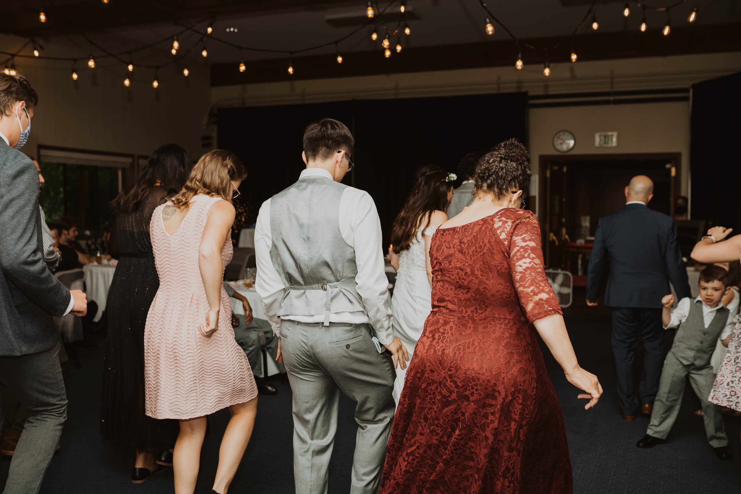 Group of people dancing at a celebration or wedding reception, with dim lighting and string lights overhead, in a decorated indoor venue. Seattle, WA wedding photography.