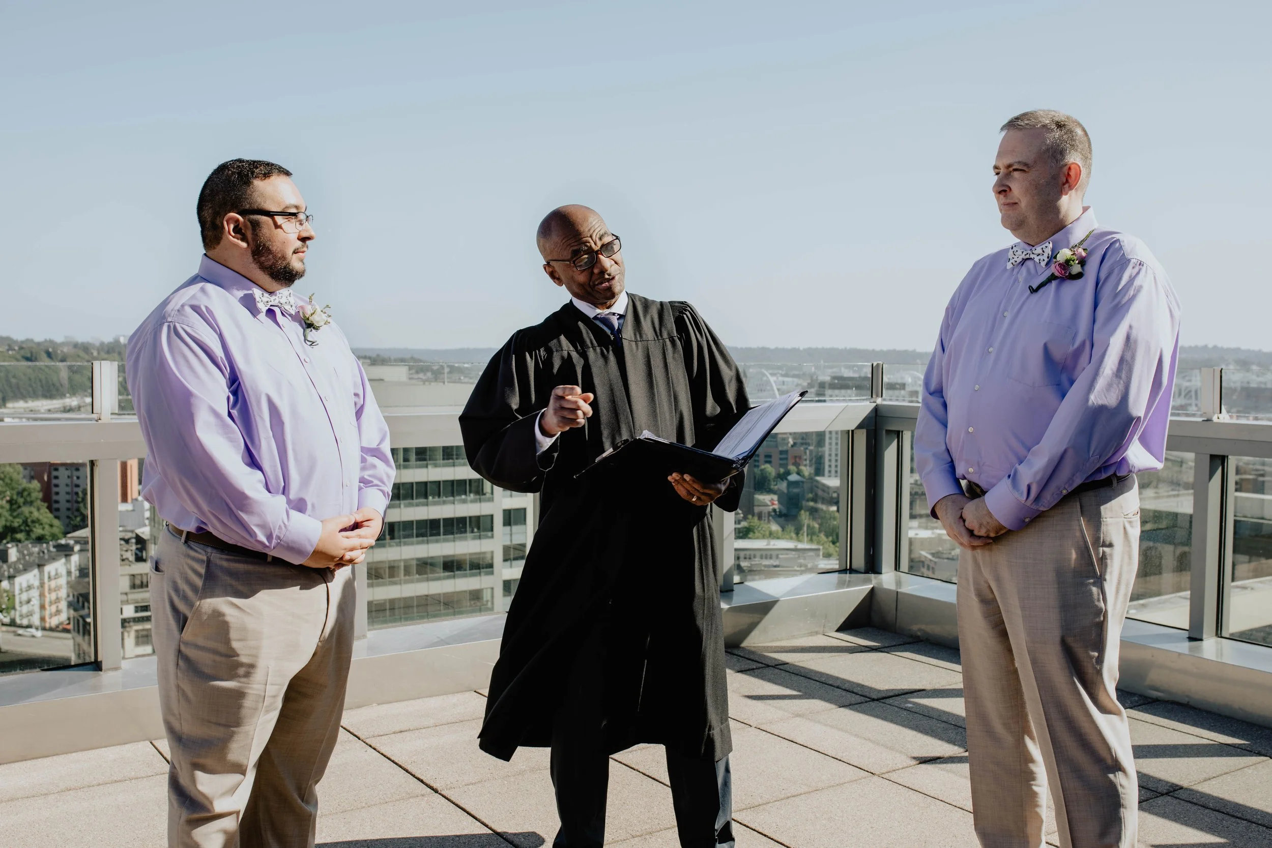 A wedding ceremony on a rooftop with two grooms and a judge officiating. Seattle Municipal Courthouse wedding photography.