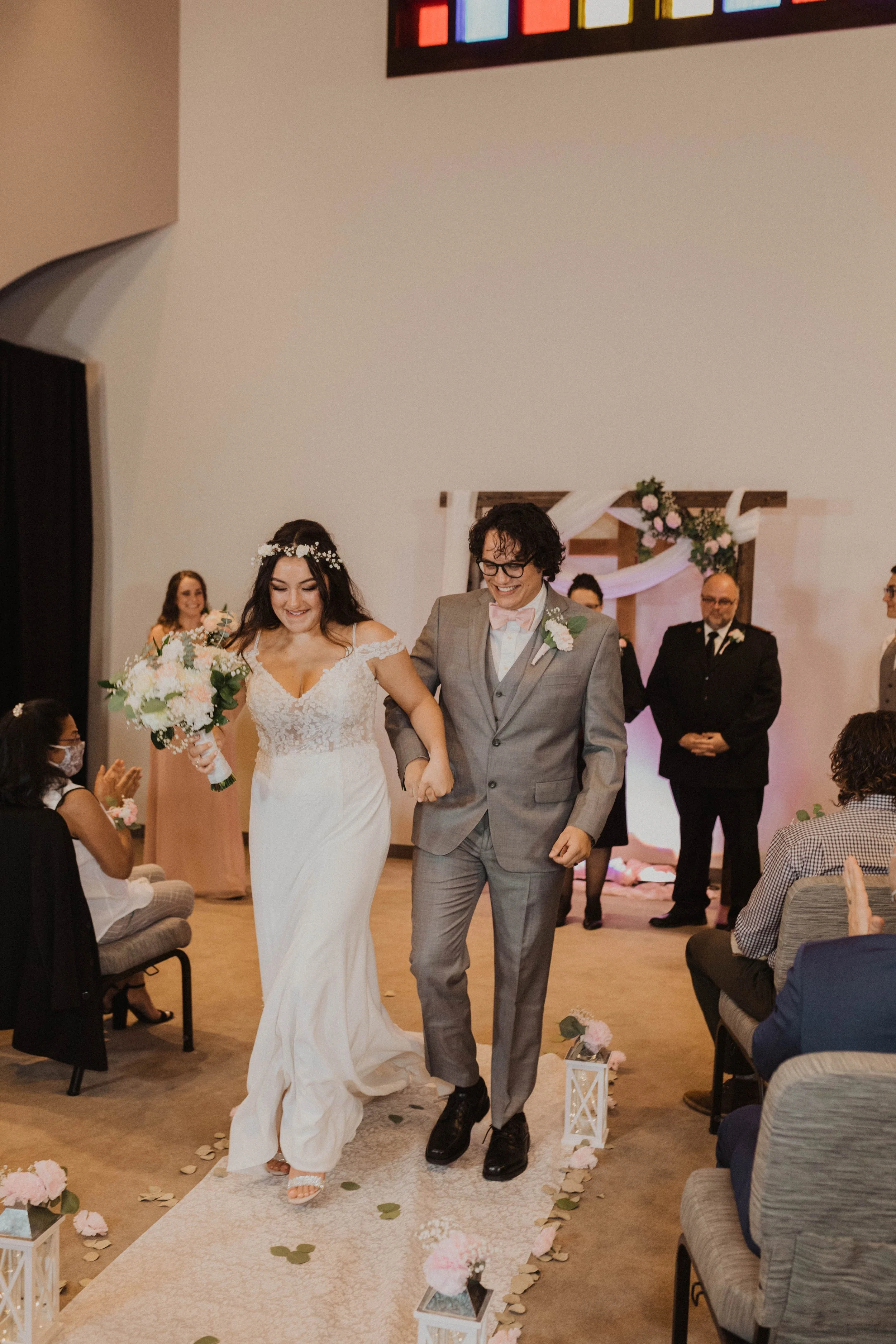 A bride and groom smiling and holding hands while walking down the aisle during their wedding ceremony, surrounded by seated guests and decorated with flowers. Seattle, WA wedding photography.