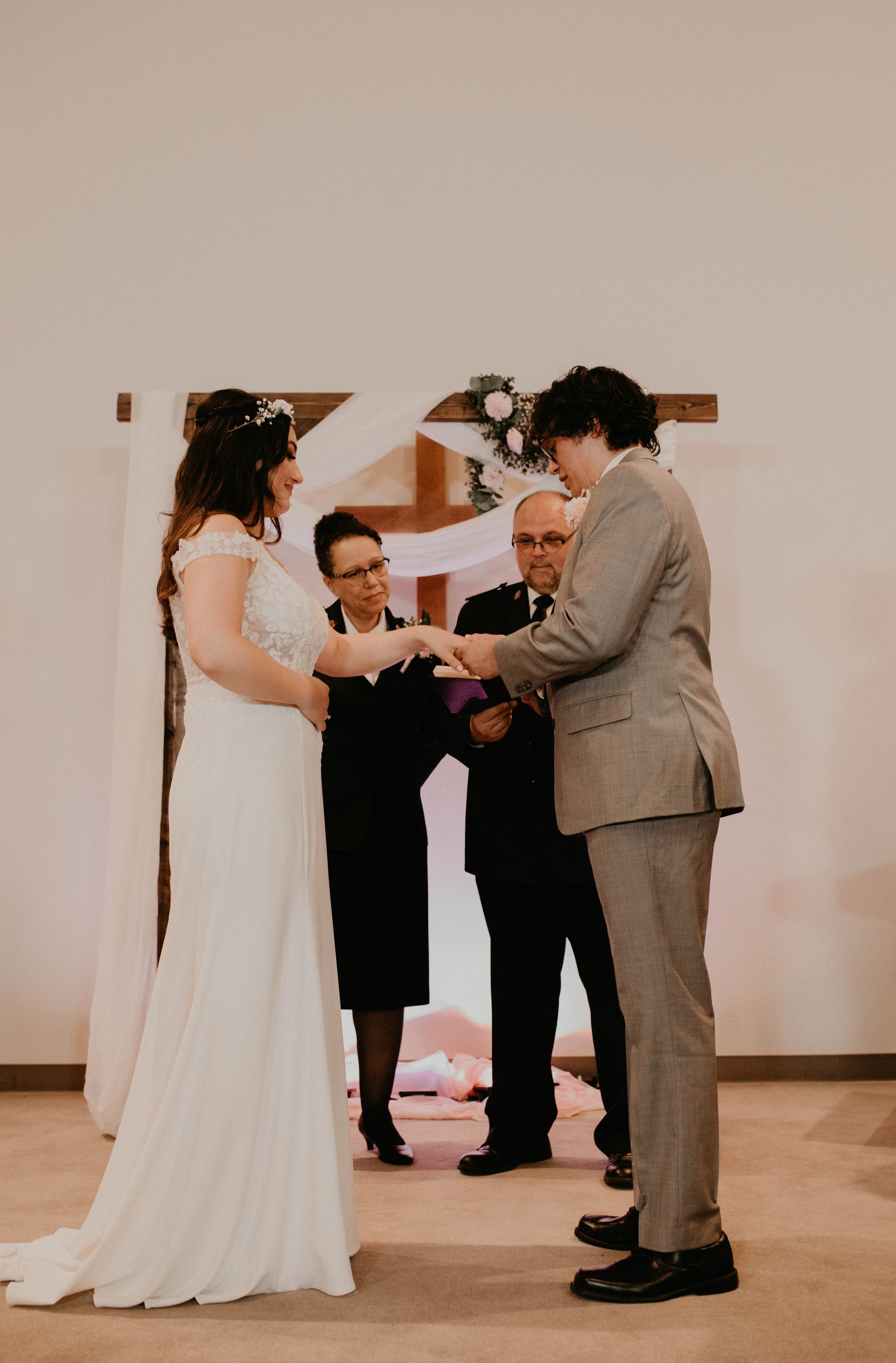 A bride and groom exchanging rings during a wedding ceremony, with two officiants or witnesses standing behind them. Seattle, WA wedding photography.