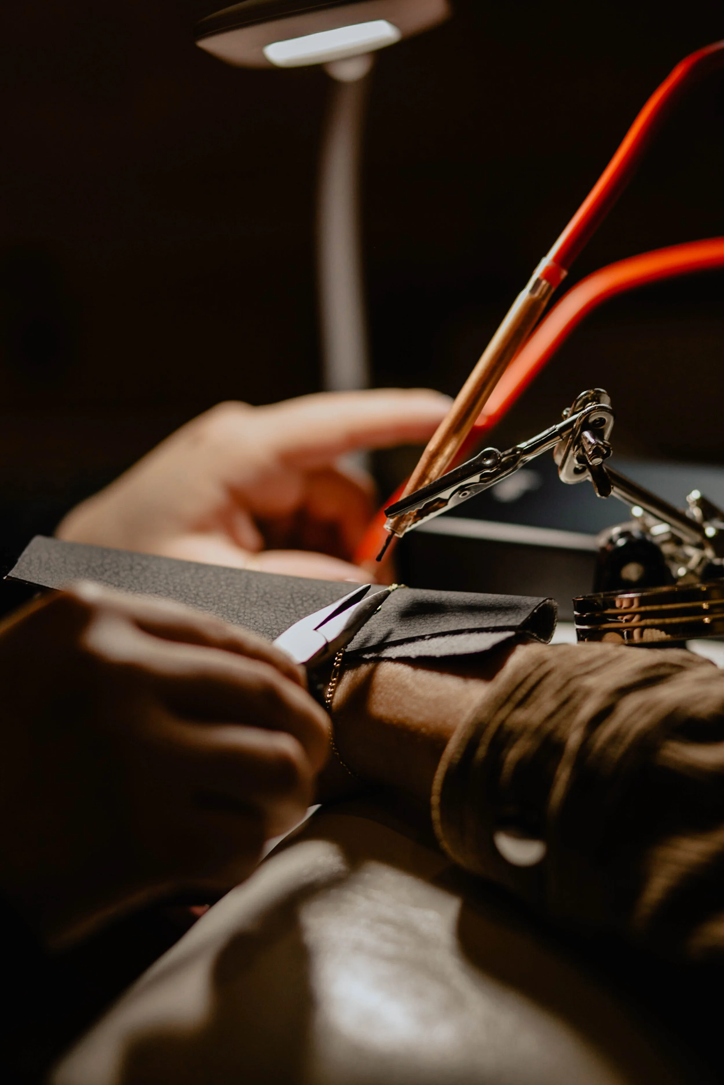 Close-up of a person using a soldering iron to work on a circuit board with tools and wires on a dark workspace. Seattle professional head shot photography
