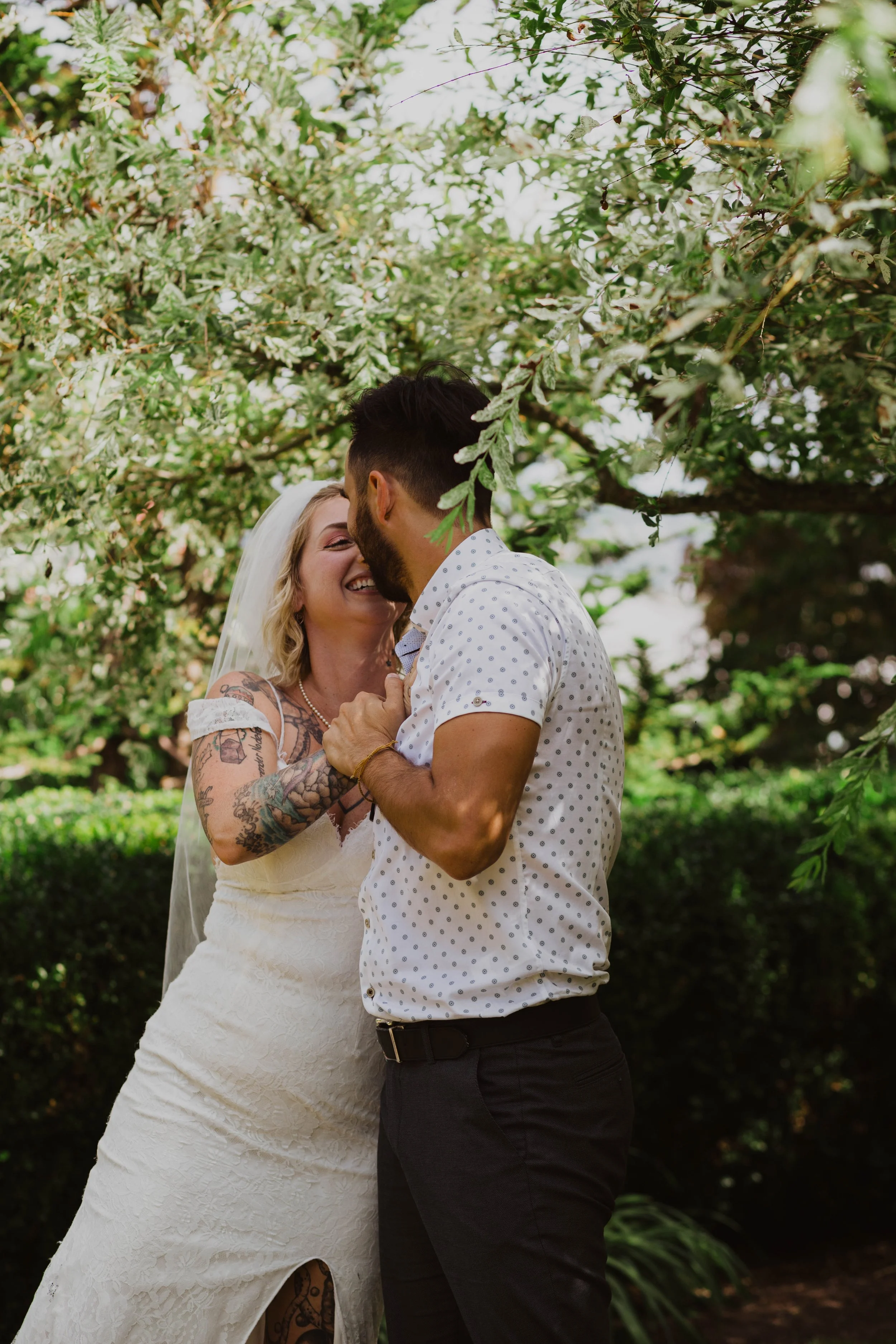 A bride and groom sharing a joyful moment outdoors under a tree, with the bride smiling and touching the groom's chest. Seattle, WA wedding photography.