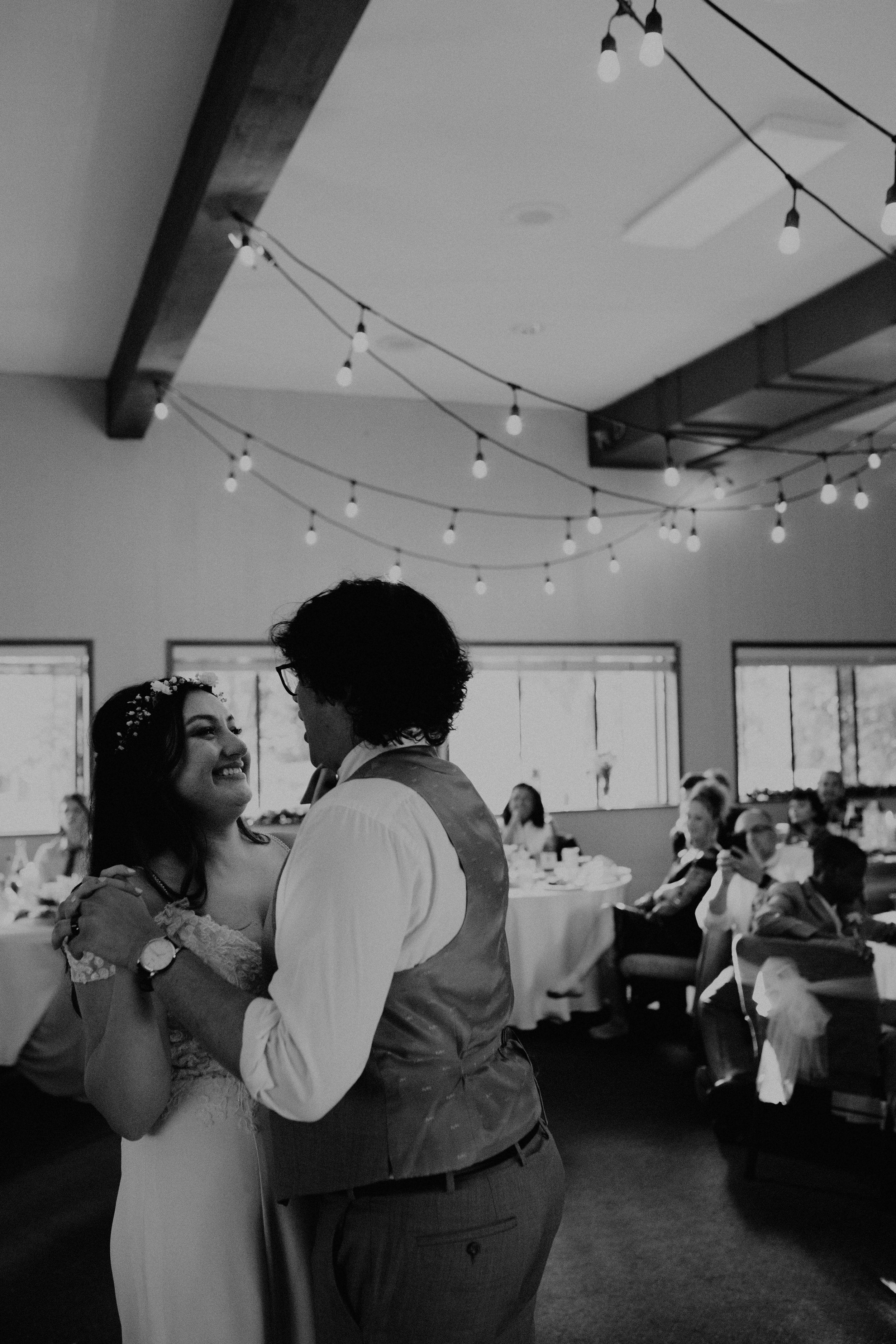 Black and white photo of a bride and groom dancing at their wedding reception, with guests watching in the background. Seattle, WA wedding photography.
