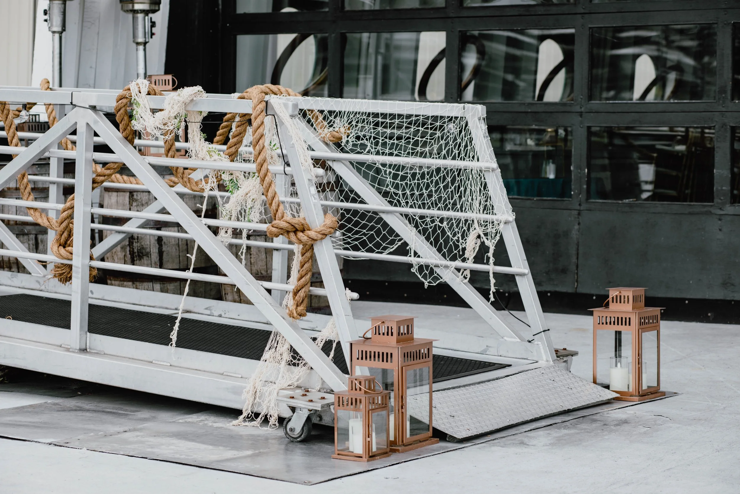 A white metal parade float with nautical ropes, fishing nets, and mesh screens, surrounded by four lanterns with candles, positioned on a concrete surface outside a building. Seattle event photography