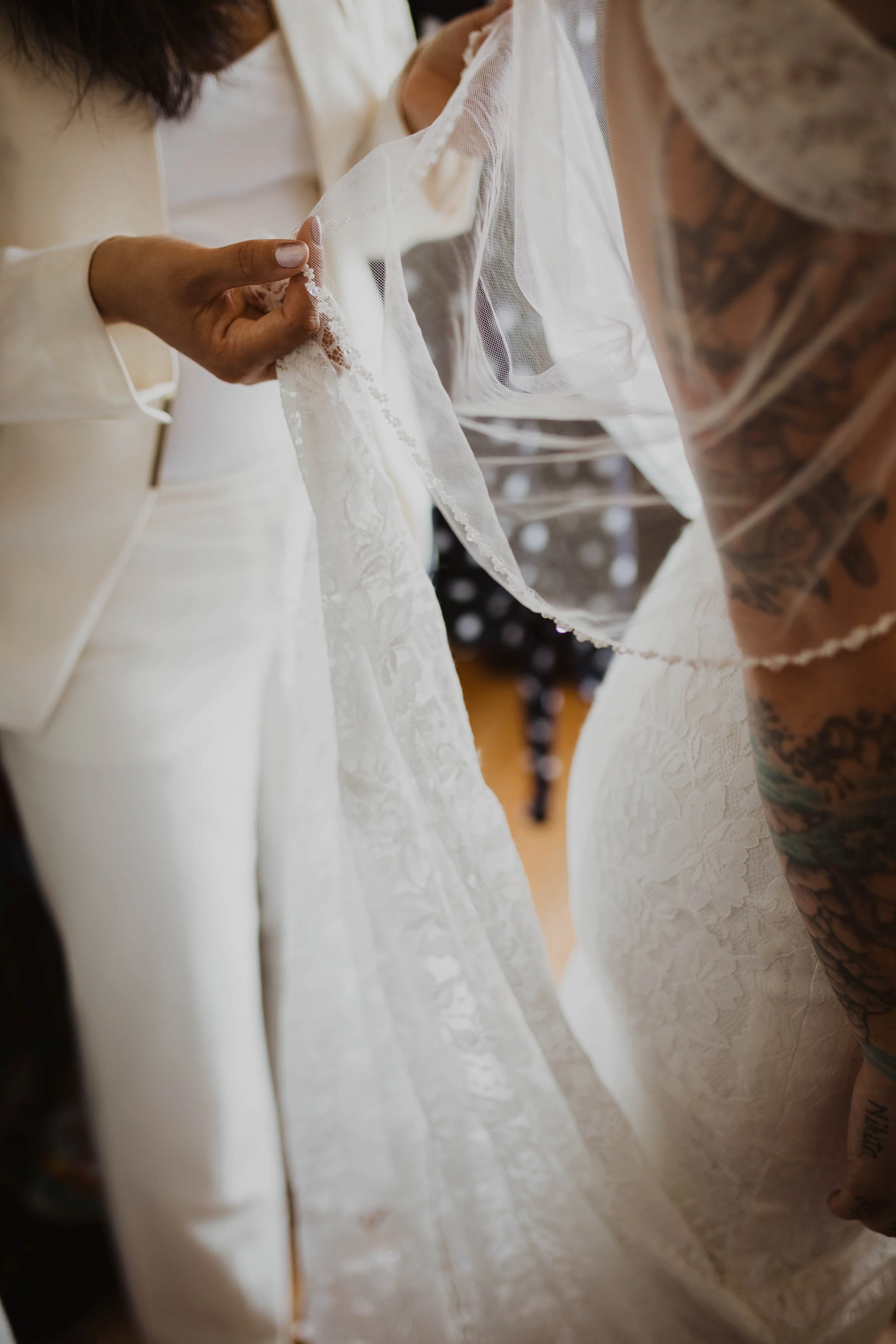 Close-up of a bride's wedding dress being handled by someone with tattoos, wearing a lace veil. Seattle, WA wedding photography.
