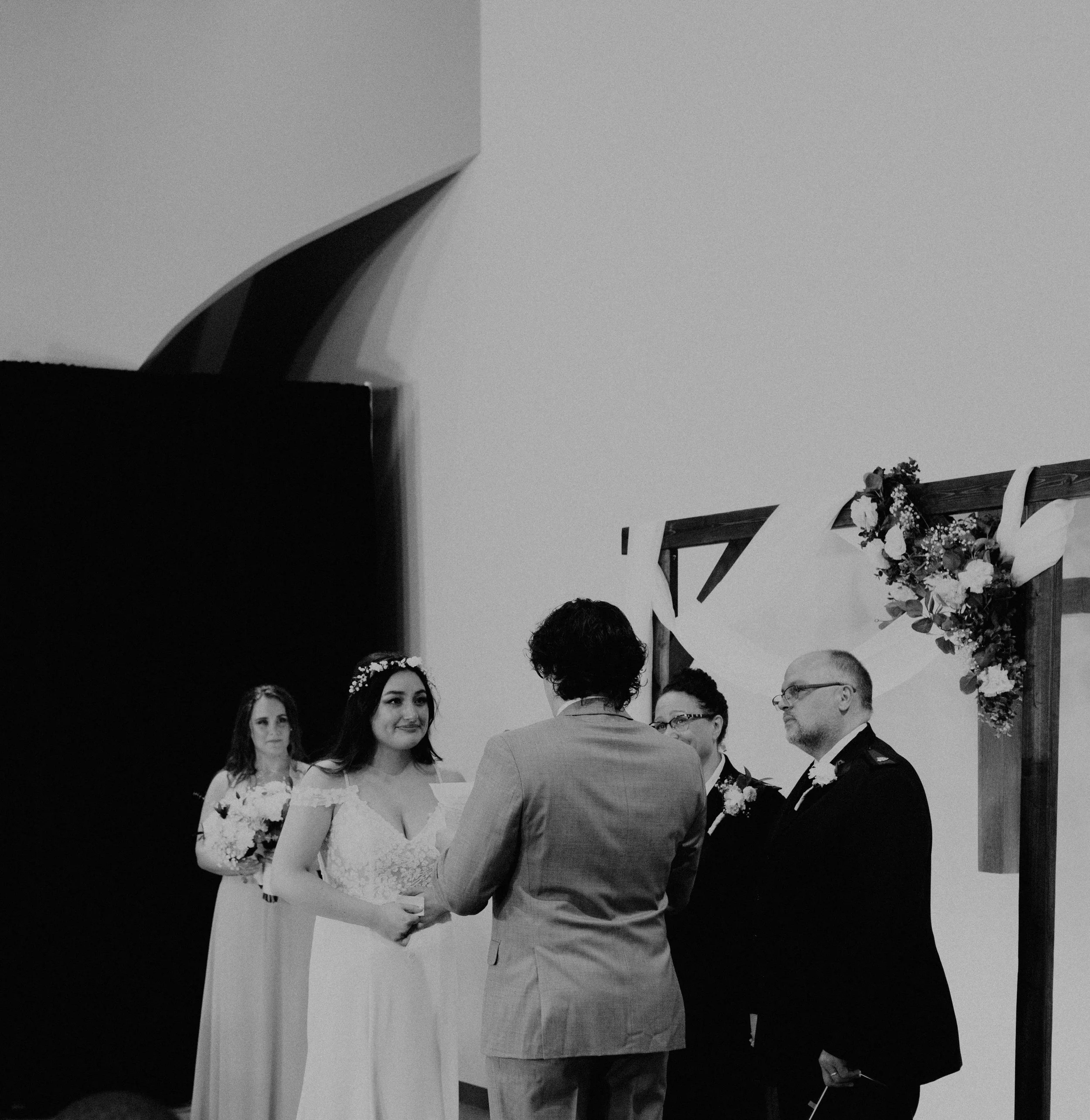 A wedding ceremony with a bride and groom exchanging vows, surrounded by two bridesmaids and two groomsmen, under a decorated arch. Seattle, WA wedding photography.
