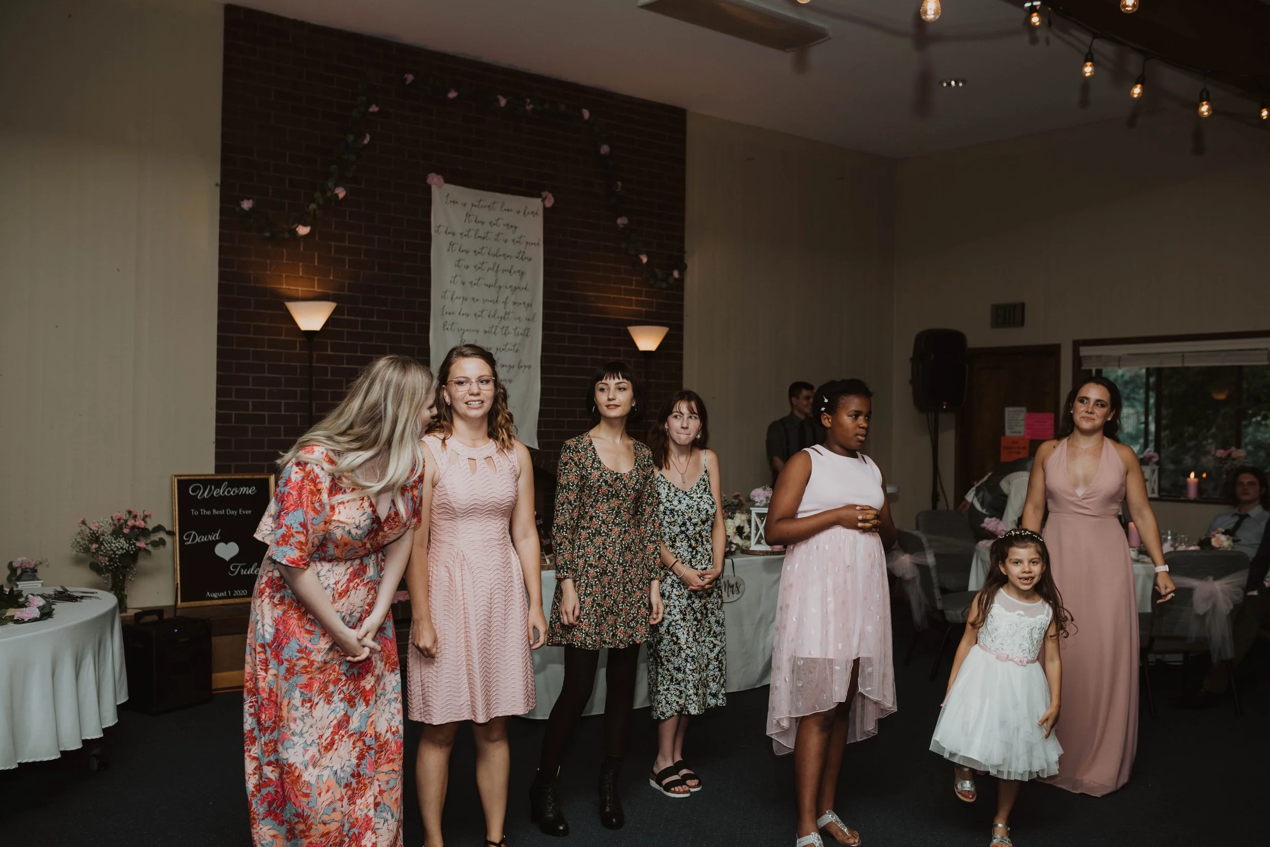 Group of women and a girl standing in a reception hall decorated with flowers, sign, and string lights, at a wedding or formal event. Seattle, WA wedding photography.