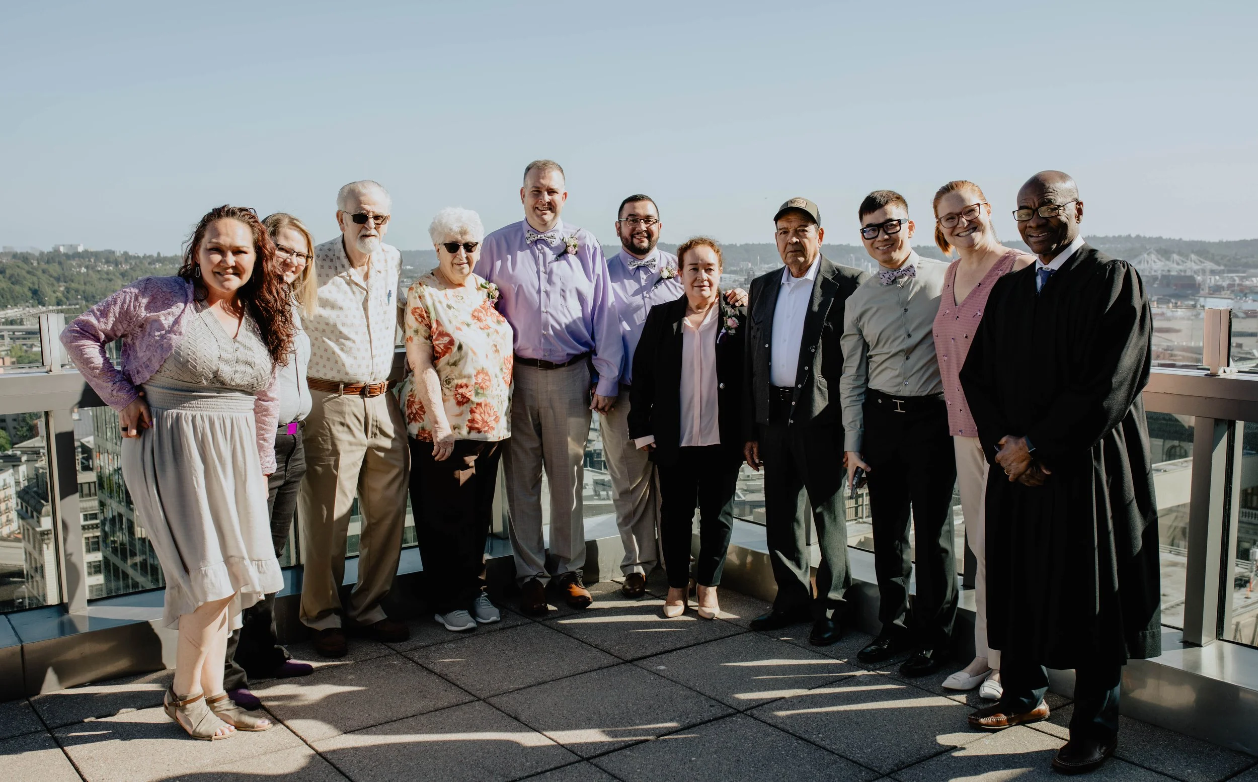 Group of people on a rooftop with a city view, dressed in semi-formal attire, celebrating a special occasion. Seattle Municipal Courthouse wedding photography.