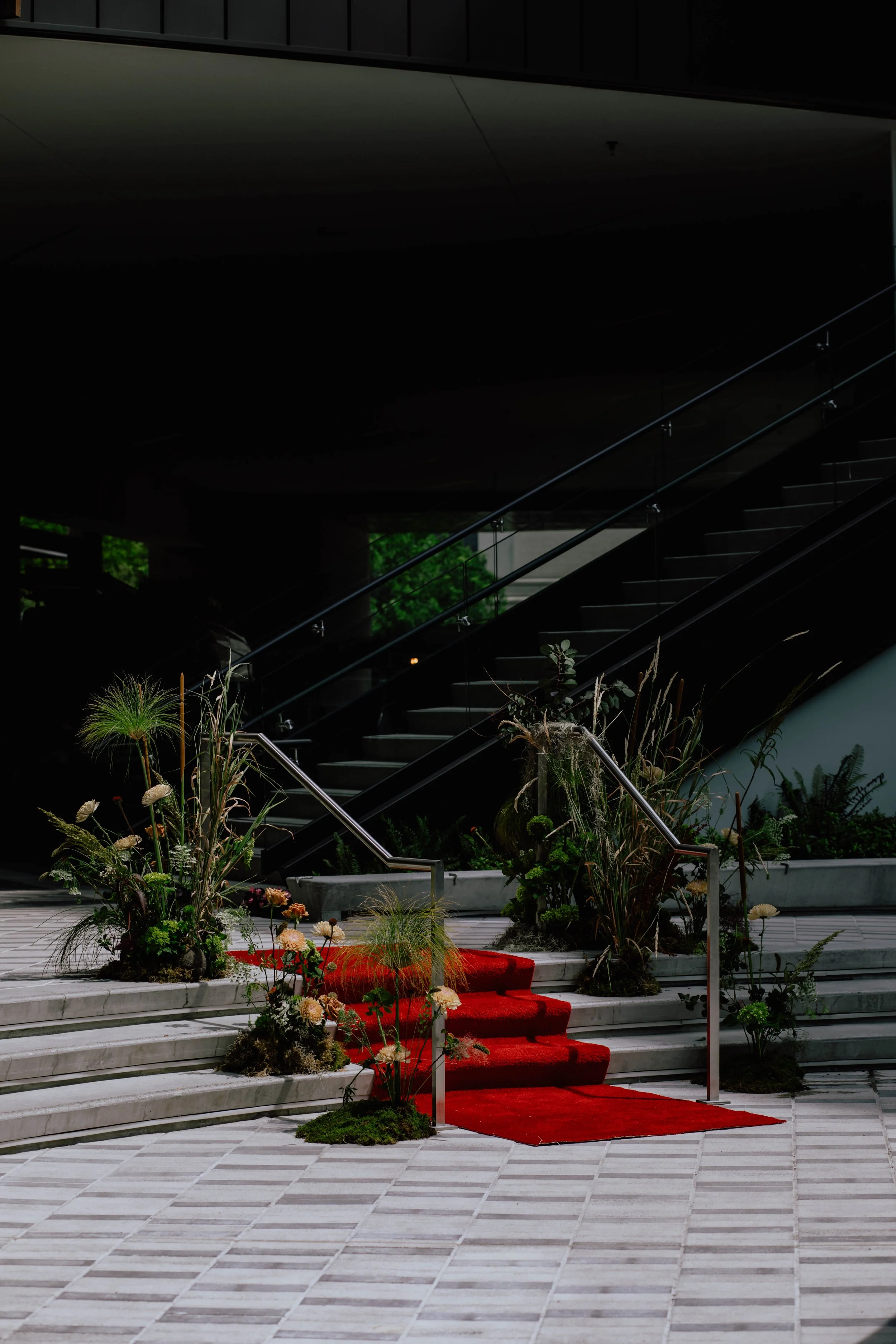 A staircase with a red carpet leading up to a modern building, decorated with plants and flowers along the sides. Seattle event photography