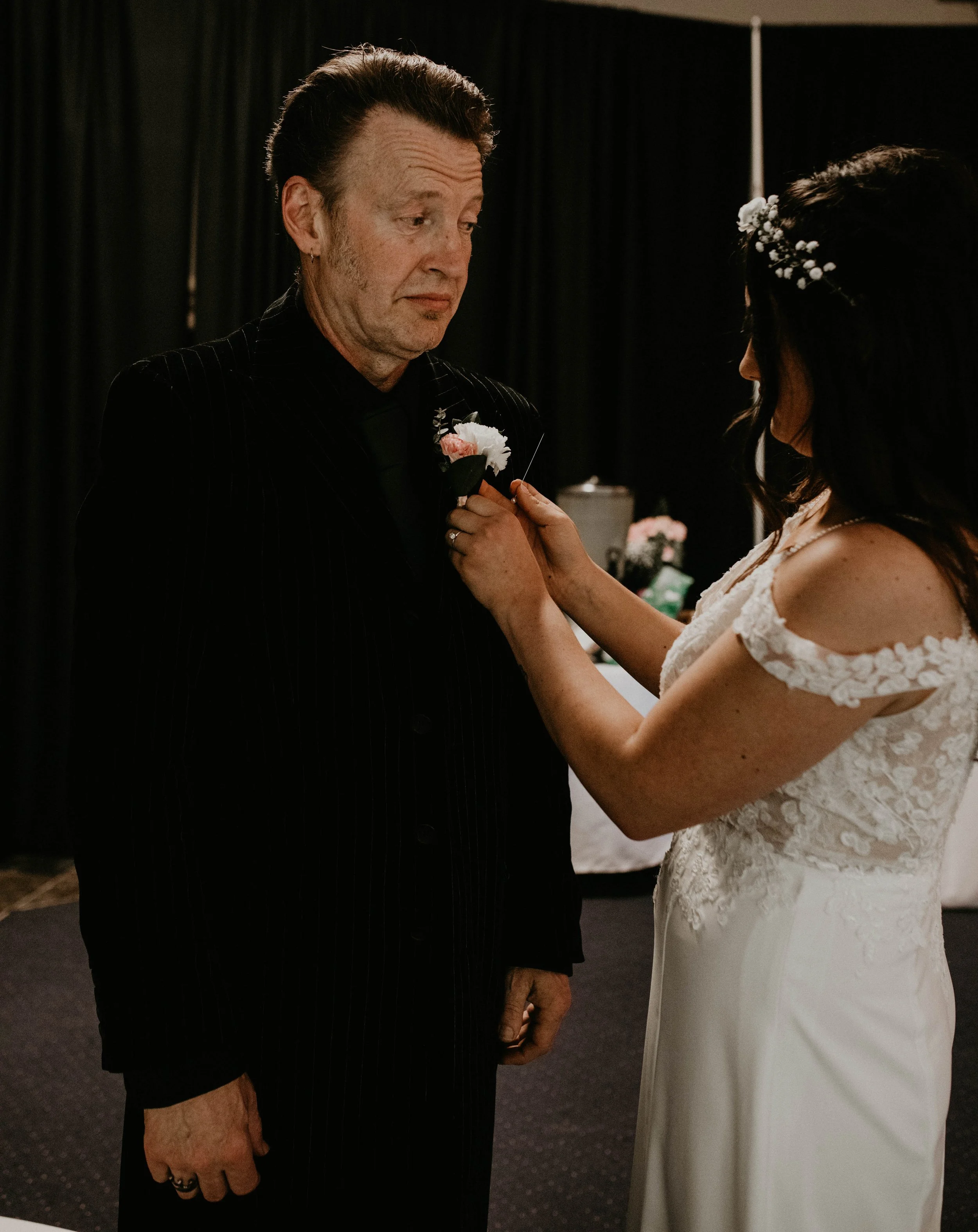 A bride pinning a pink and white boutonniere onto an older man at a wedding reception. Seattle, WA wedding photography.