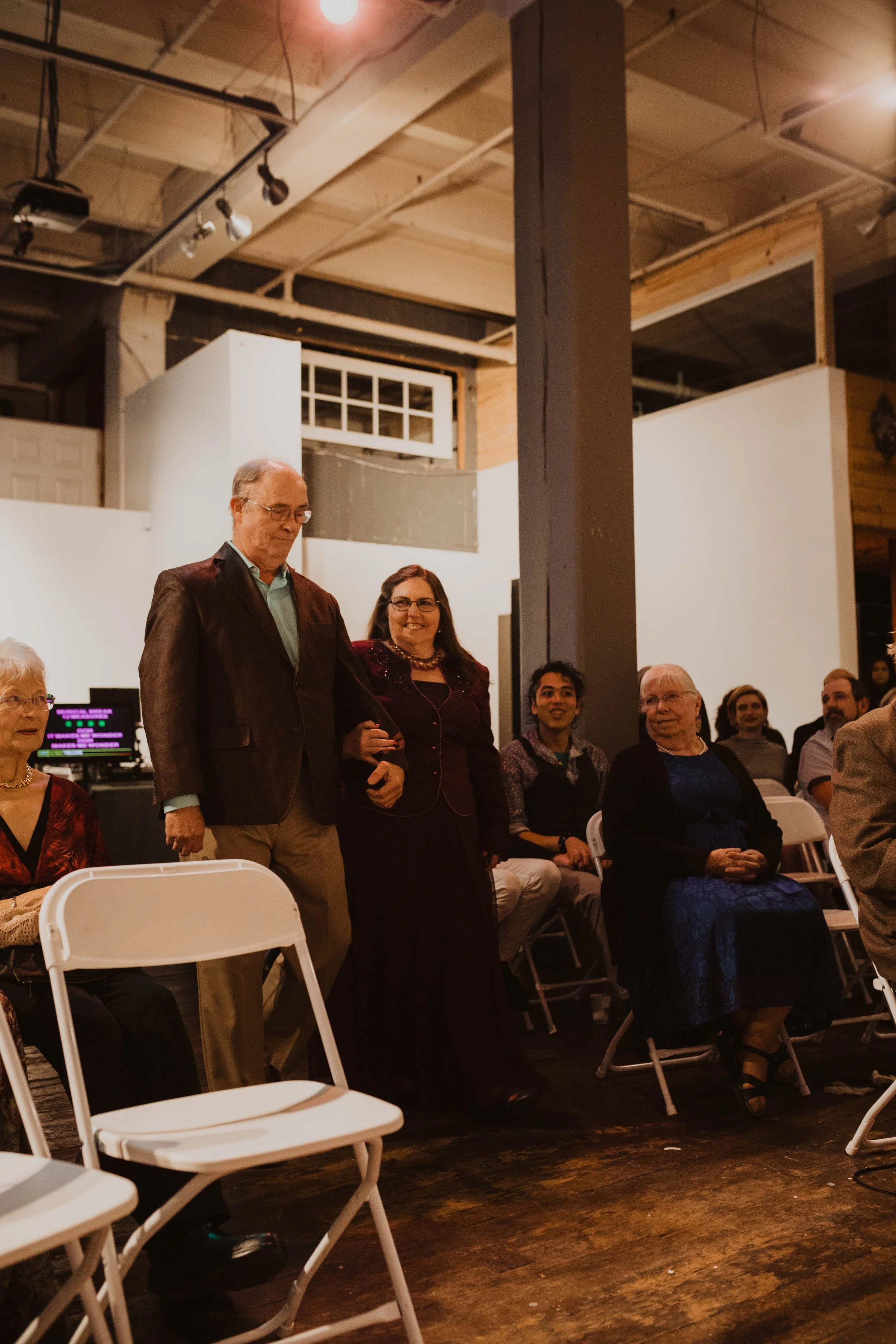 Group of adults sitting and standing in a large indoor space, likely at an event or gathering, with some smiling and engaged. Pioneer Square, Seattle, WA wedding photography.