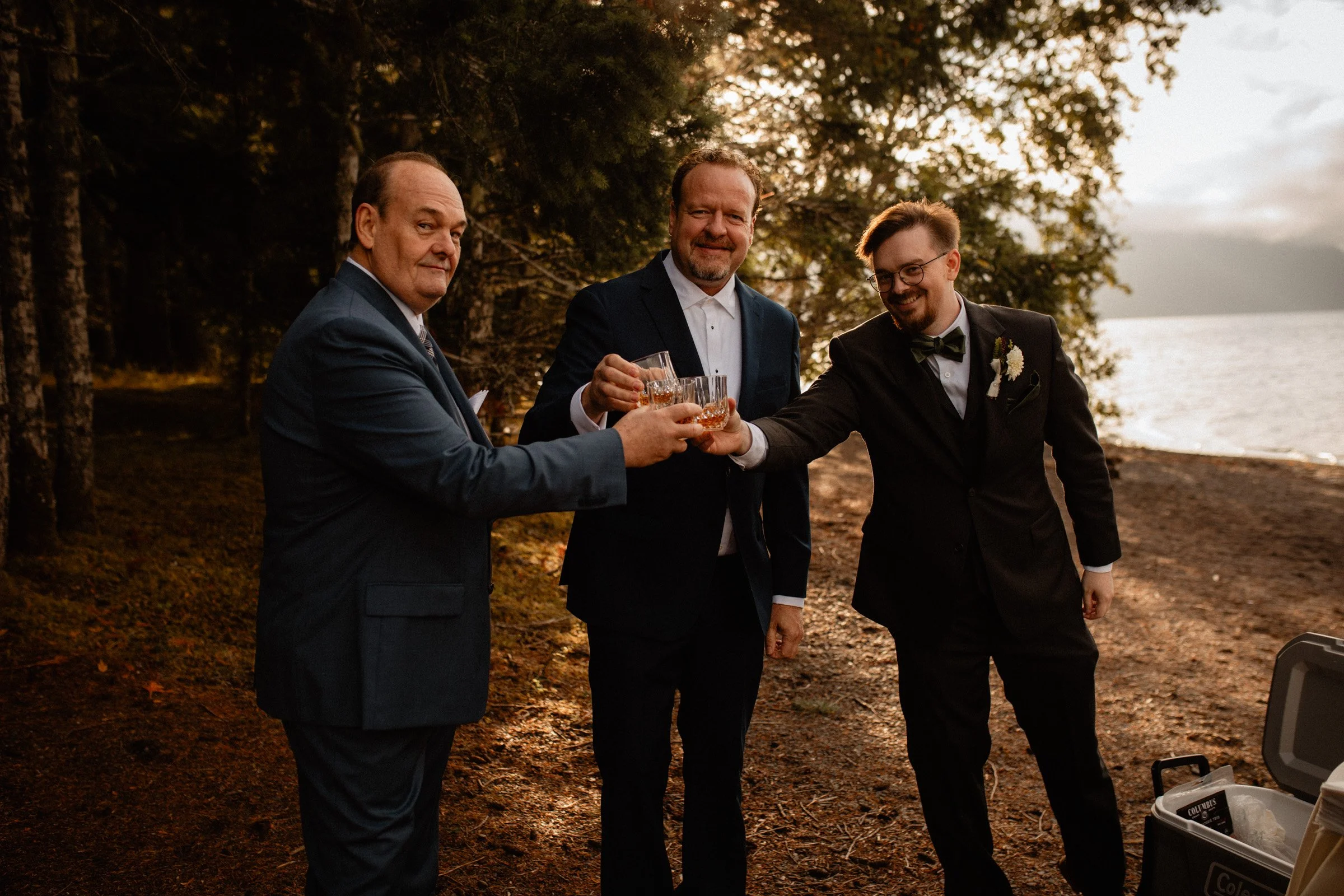 Father of the groom, father of the bride, and the groom clinking glasses and smiling during the Lake Crescent Lodge wedding in Port Angeles, WA.