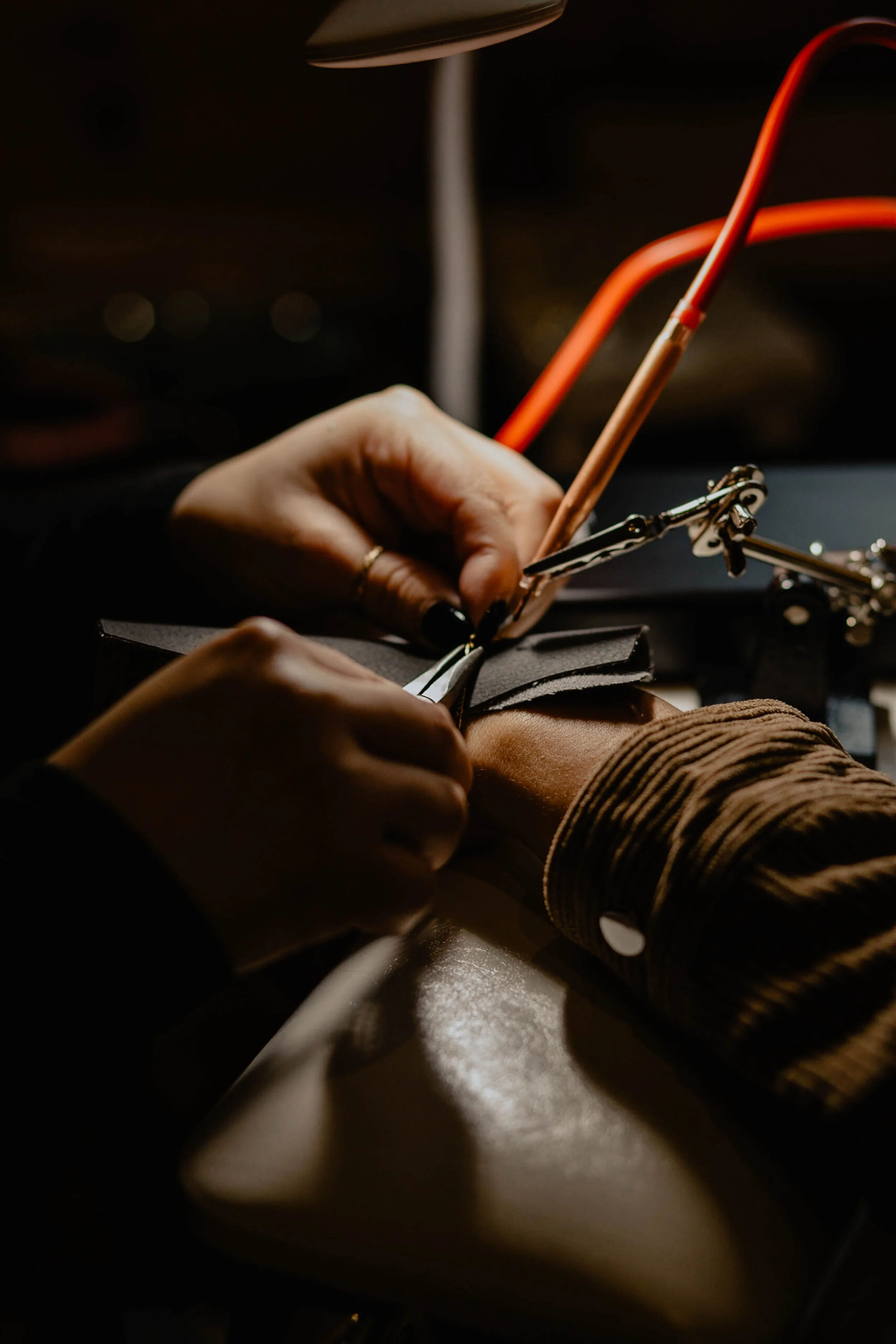 Close-up of a person working on a leather project, using tools and wire to assemble or repair leather, with a focused hand and workspace illuminated in warm light. Seattle professional head shot photography