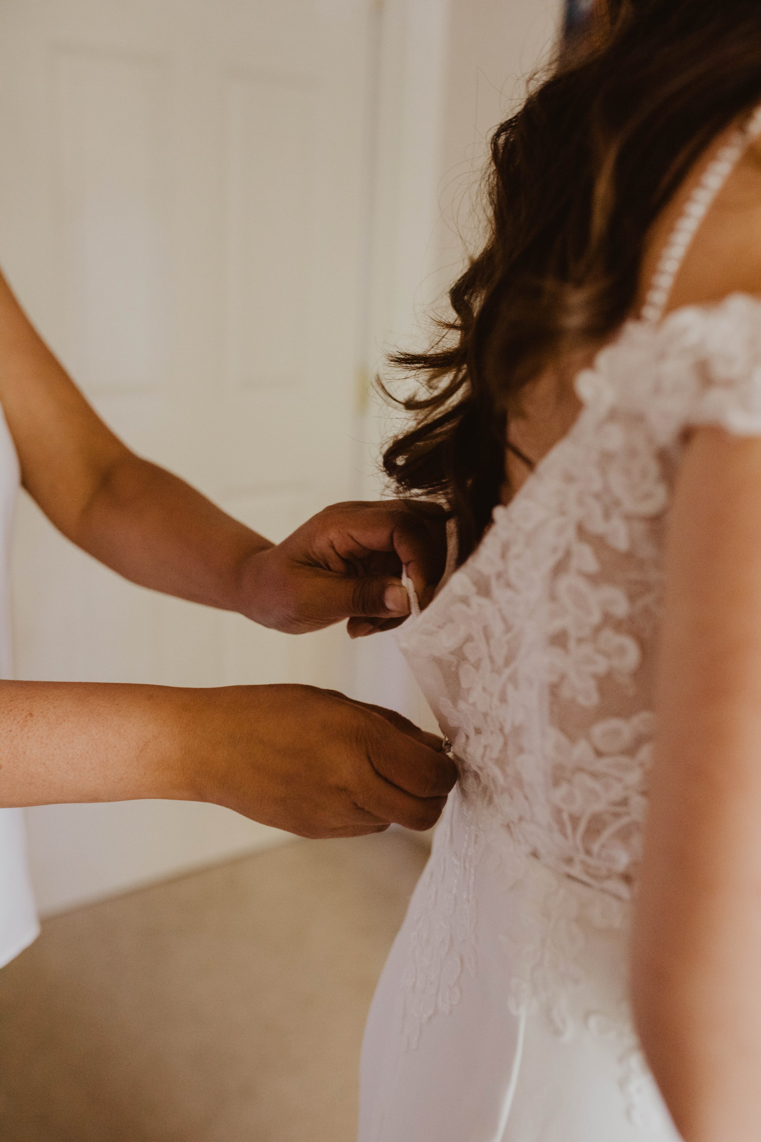 Person fastening the back clasp of a white lace wedding dress. Seattle, WA wedding photography.