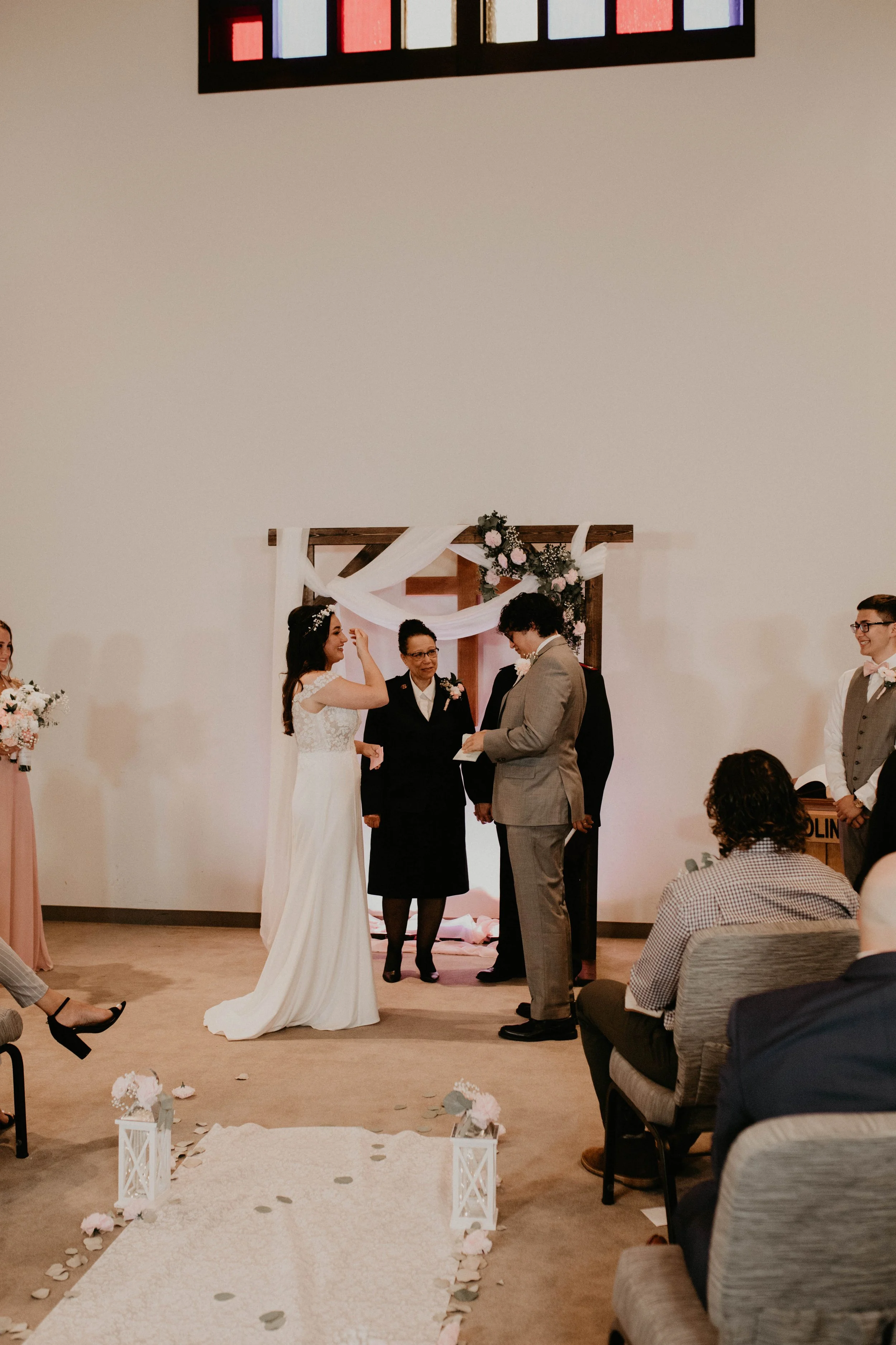A wedding ceremony with a bride and groom standing under an arch as they exchange vows, surrounded by officiant and wedding party, inside a decorated room with an aisle decorated with flowers and lanterns. Seattle, WA wedding photography.