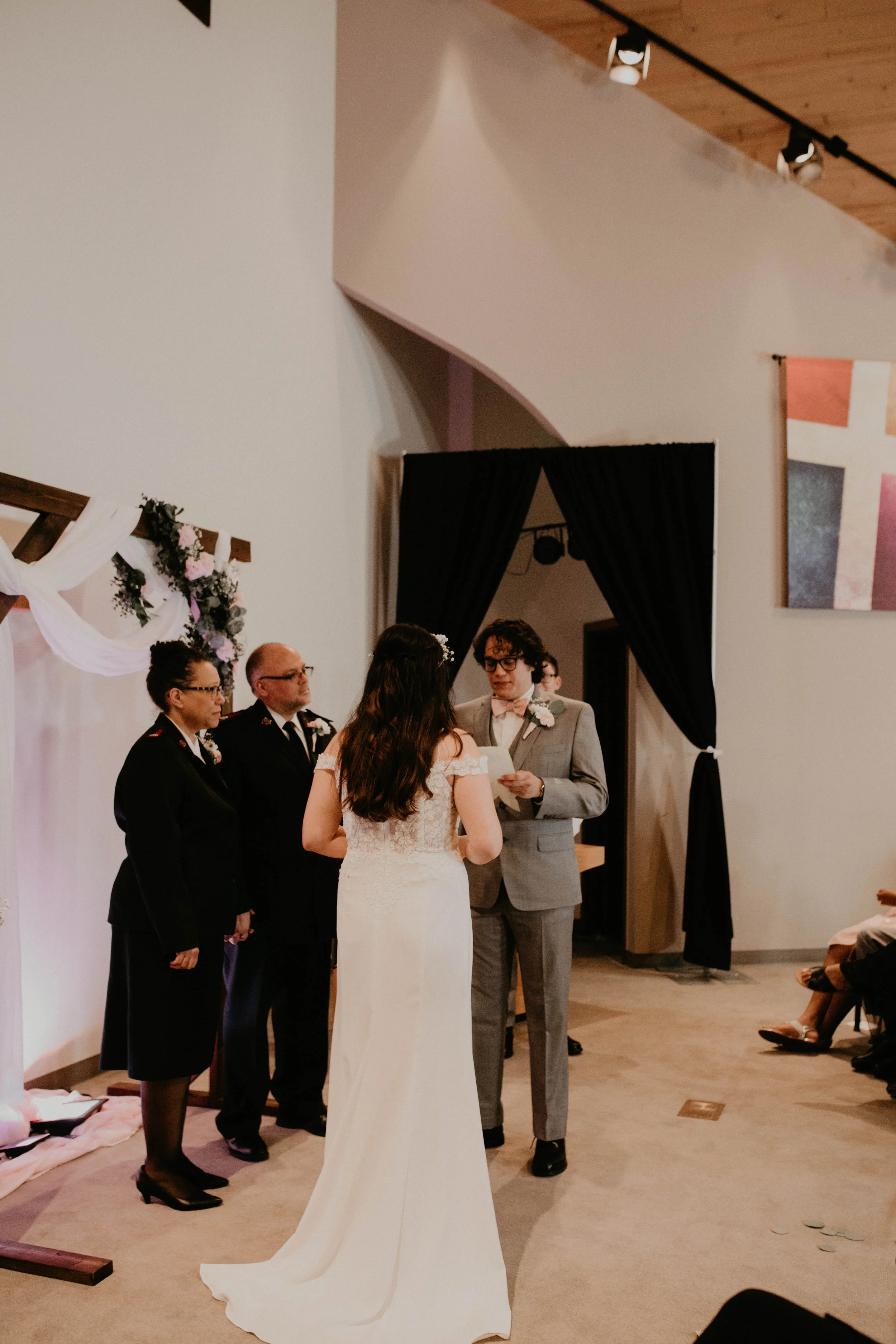 A wedding ceremony with the bride and groom exchanging vows in front of officiant, with witnesses standing nearby in a decorated indoor setting. Seattle, WA wedding photography.