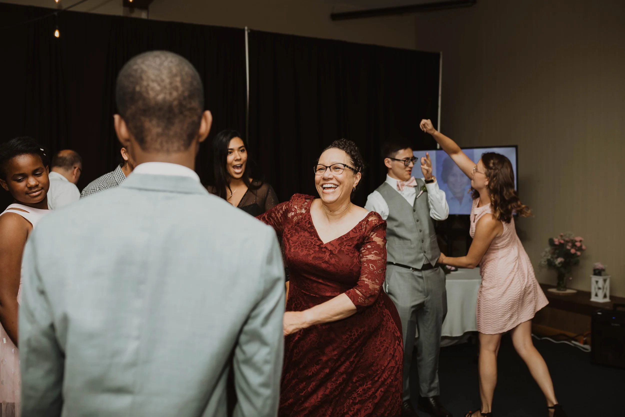 People dancing and celebrating at a party, with a woman in a red dress smiling in the center. Seattle, WA wedding photography.