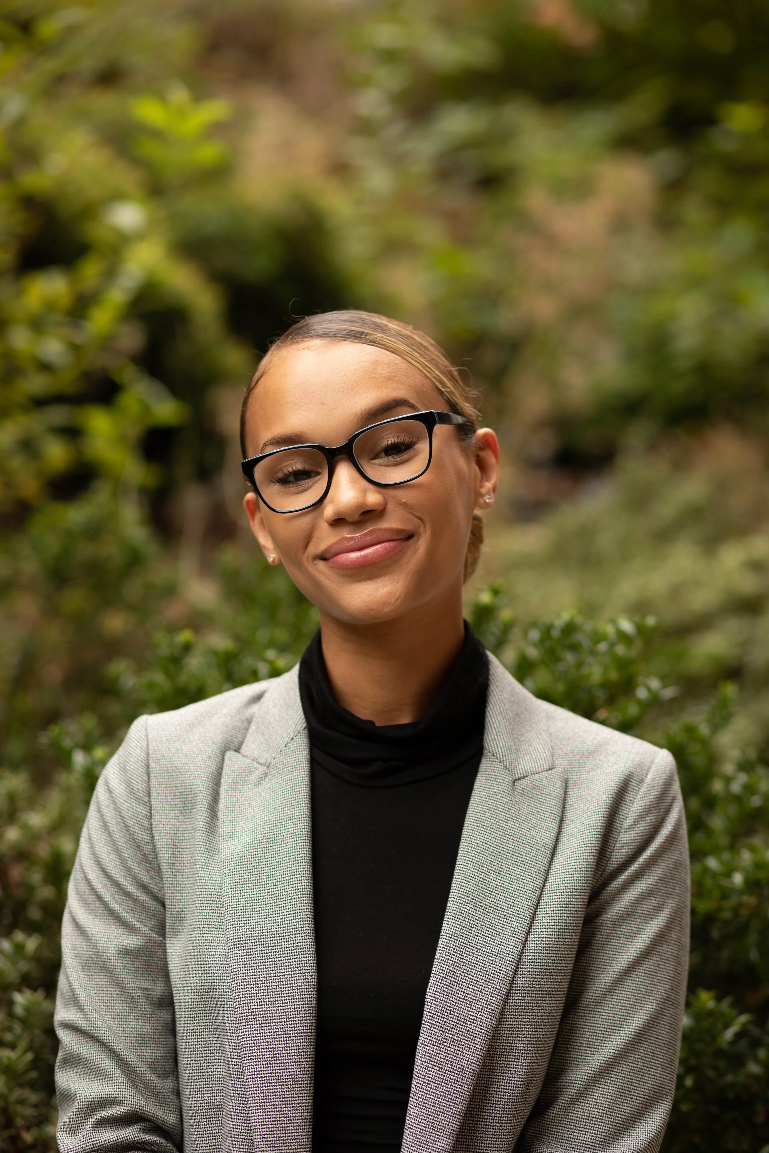 A young woman with glasses and a blazer smiling outdoors. Seattle professional head shot photography