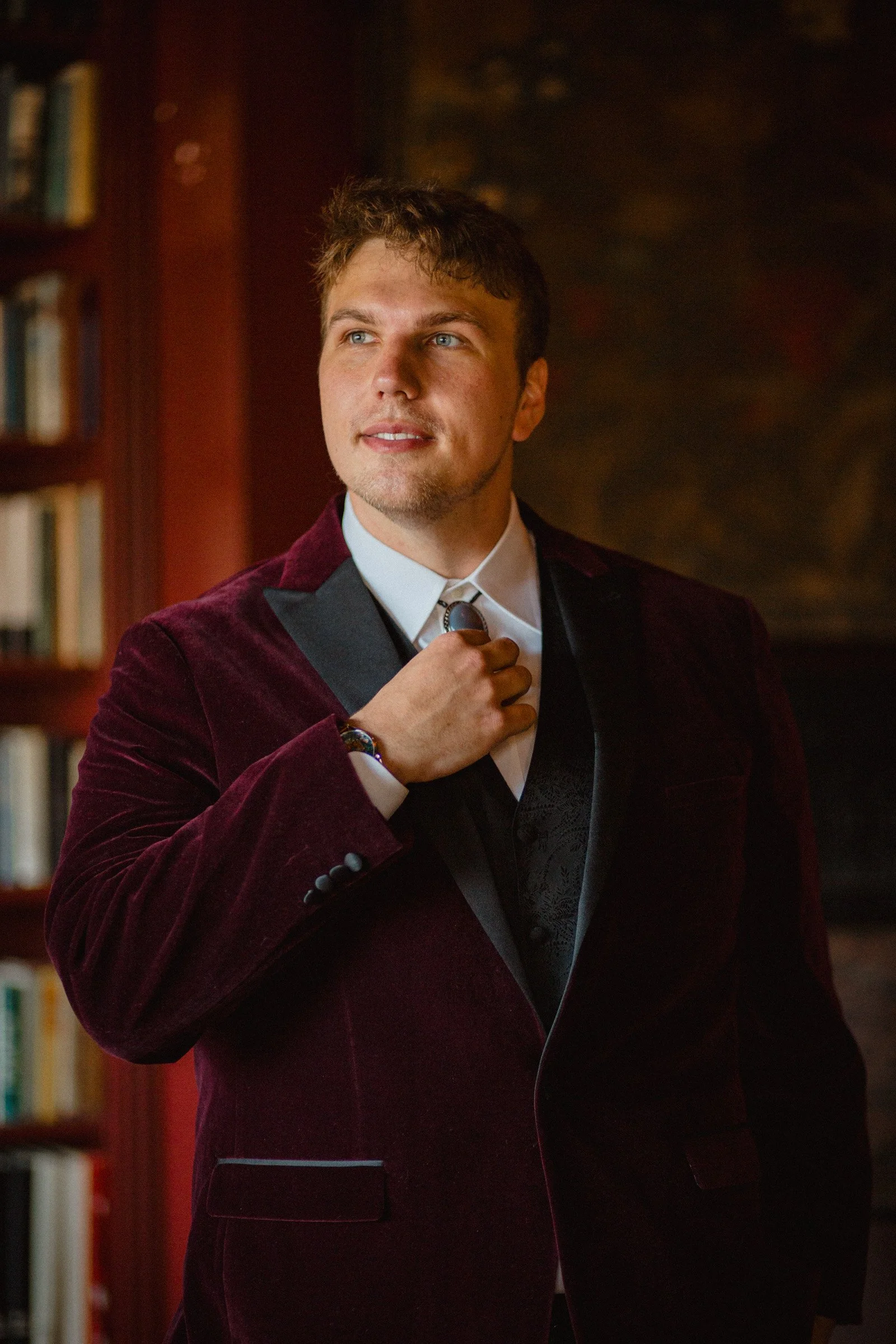 Groom adjusts his tie in the library of The Ruins, Queen Anne, Seattle