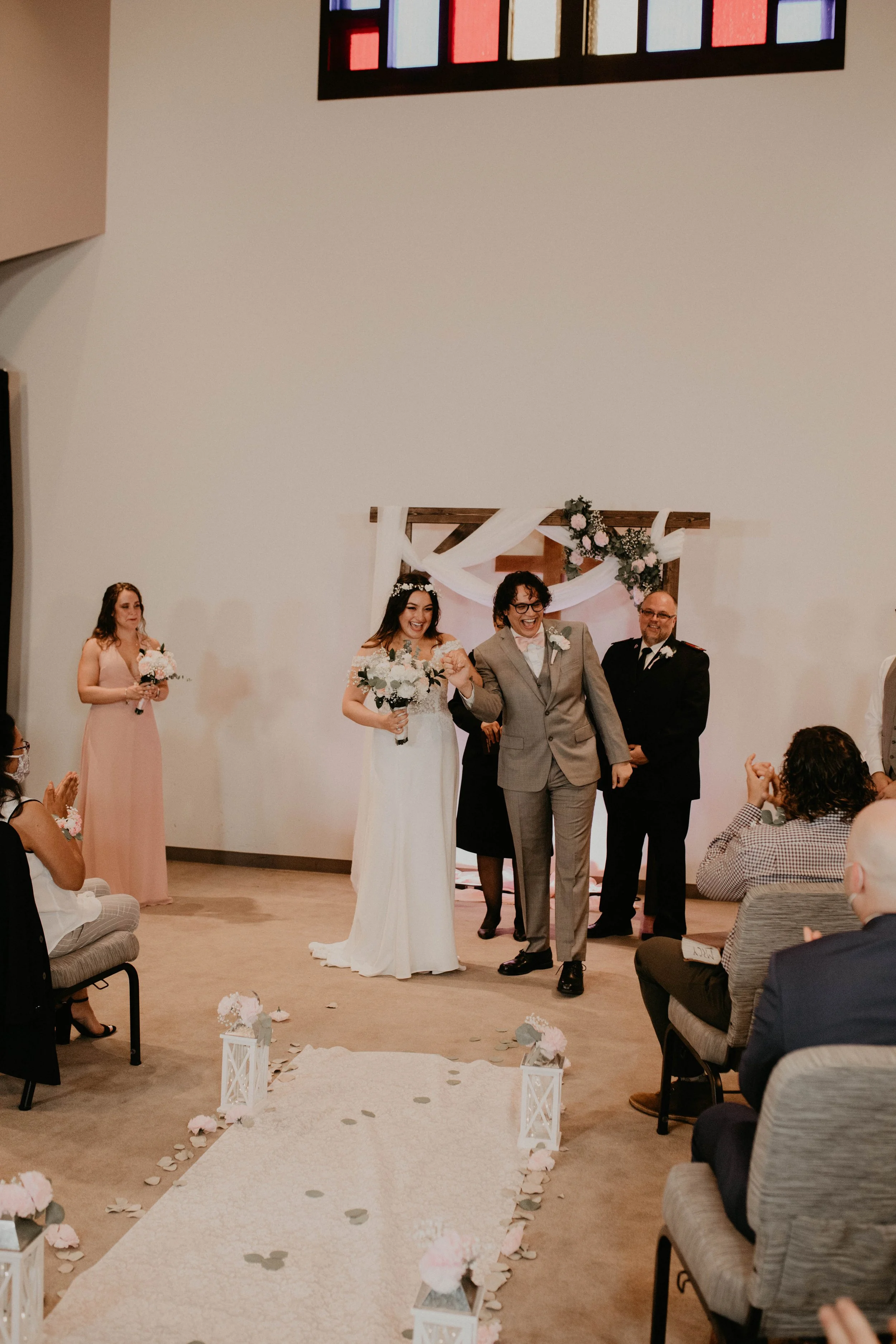 A bride and a man, possibly her father, smiling and holding hands as they walk down the aisle at a wedding ceremony, with guests seated on either side. Seattle, WA wedding photography.