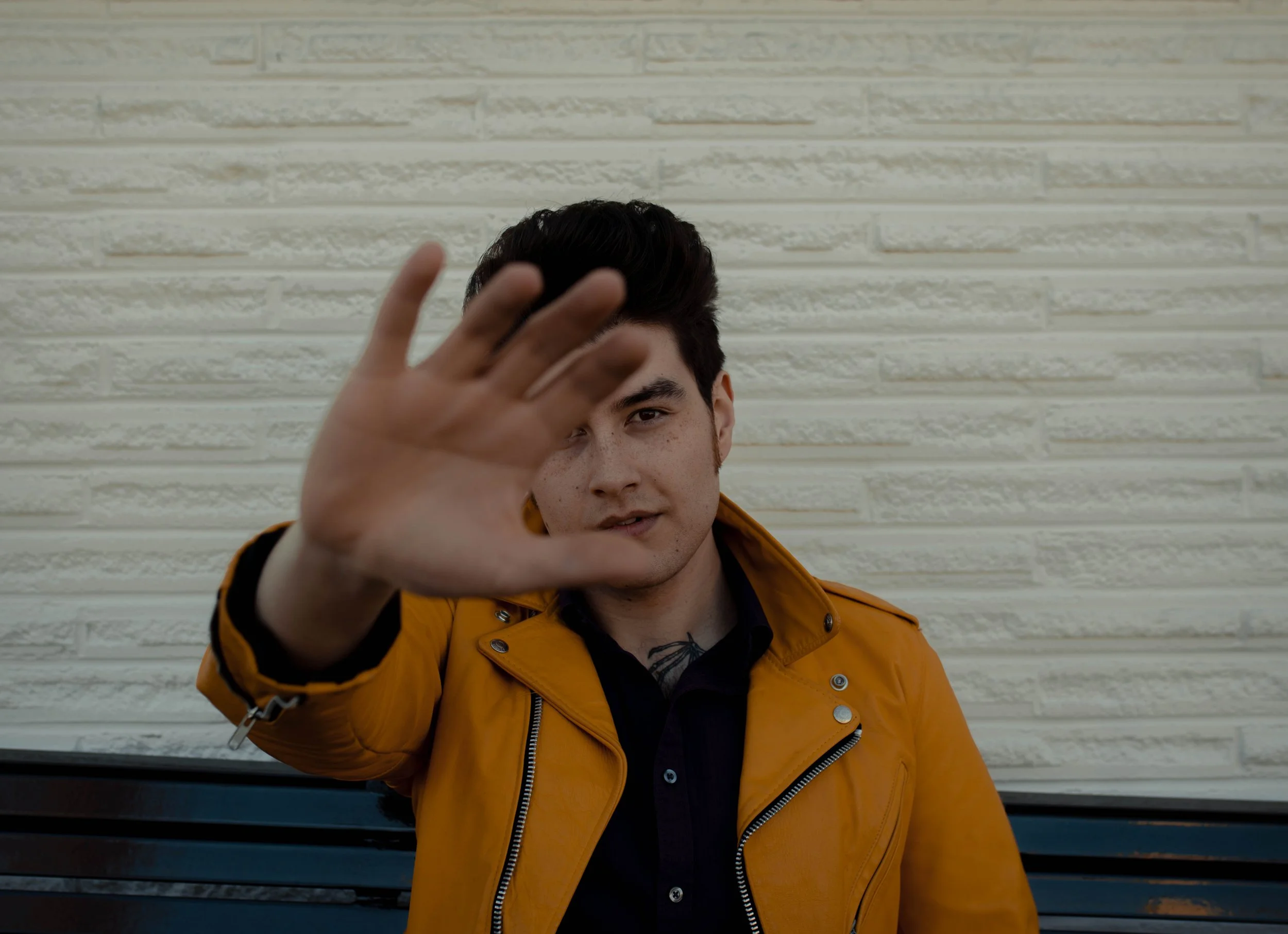 Young man in a yellow jacket sitting outdoors, reaching towards the camera with his hand. Seattle professional head shot photography