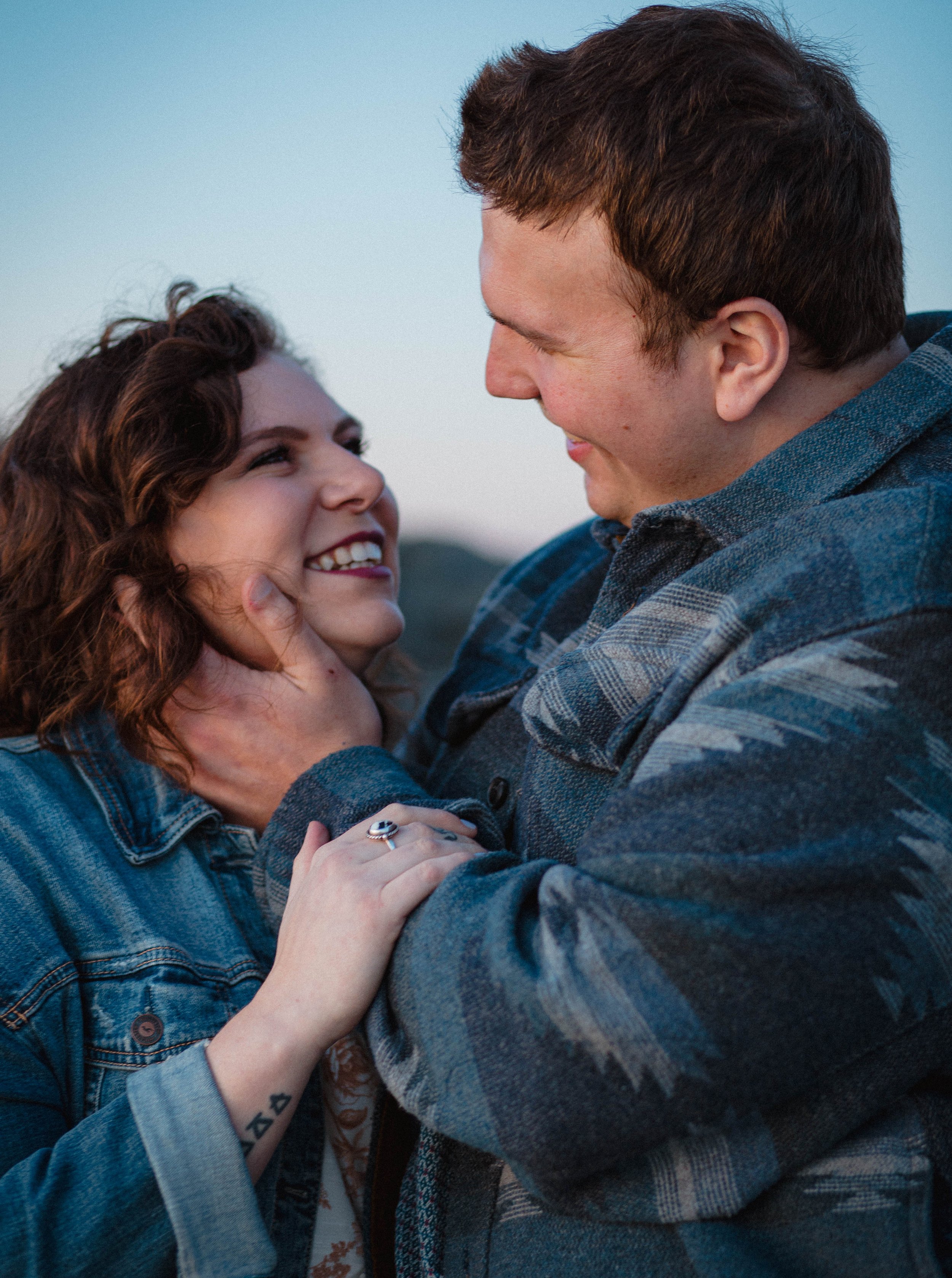 A couple embraces in a close up image taken at blue honor on Edmonds beach. The couple is celebrating their engagement.