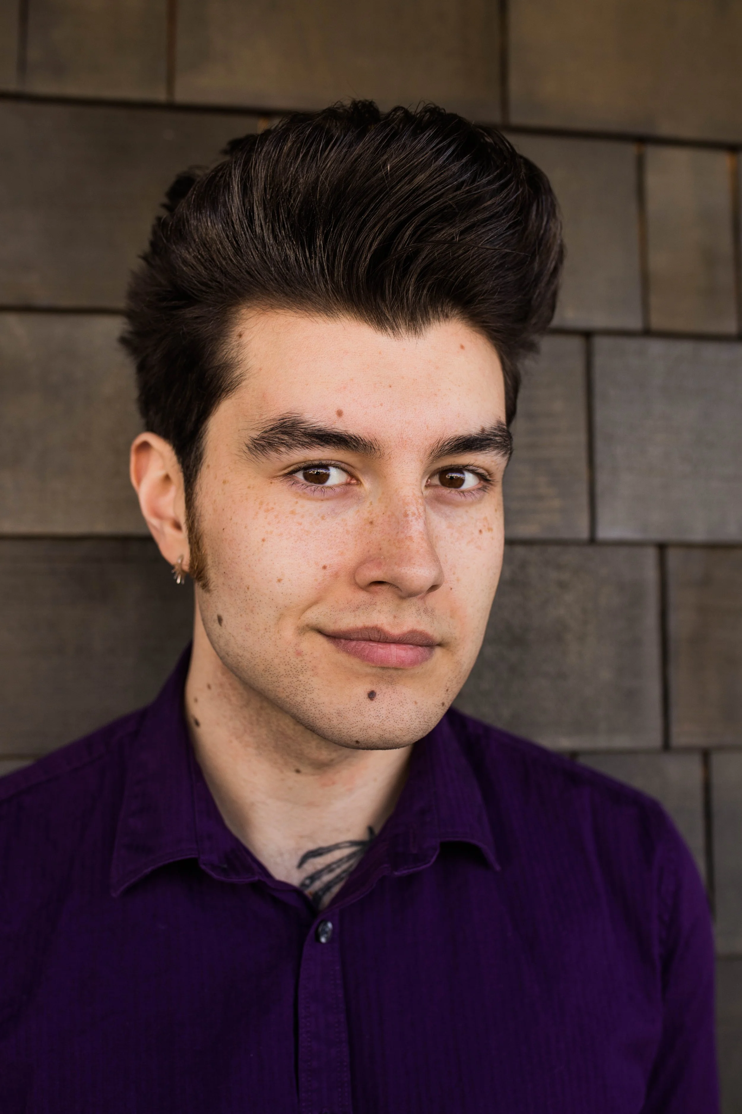 Portrait of a young man with dark hair styled back, wearing a purple shirt, standing against a dark wood-paneled wall. Seattle professional head shot photography