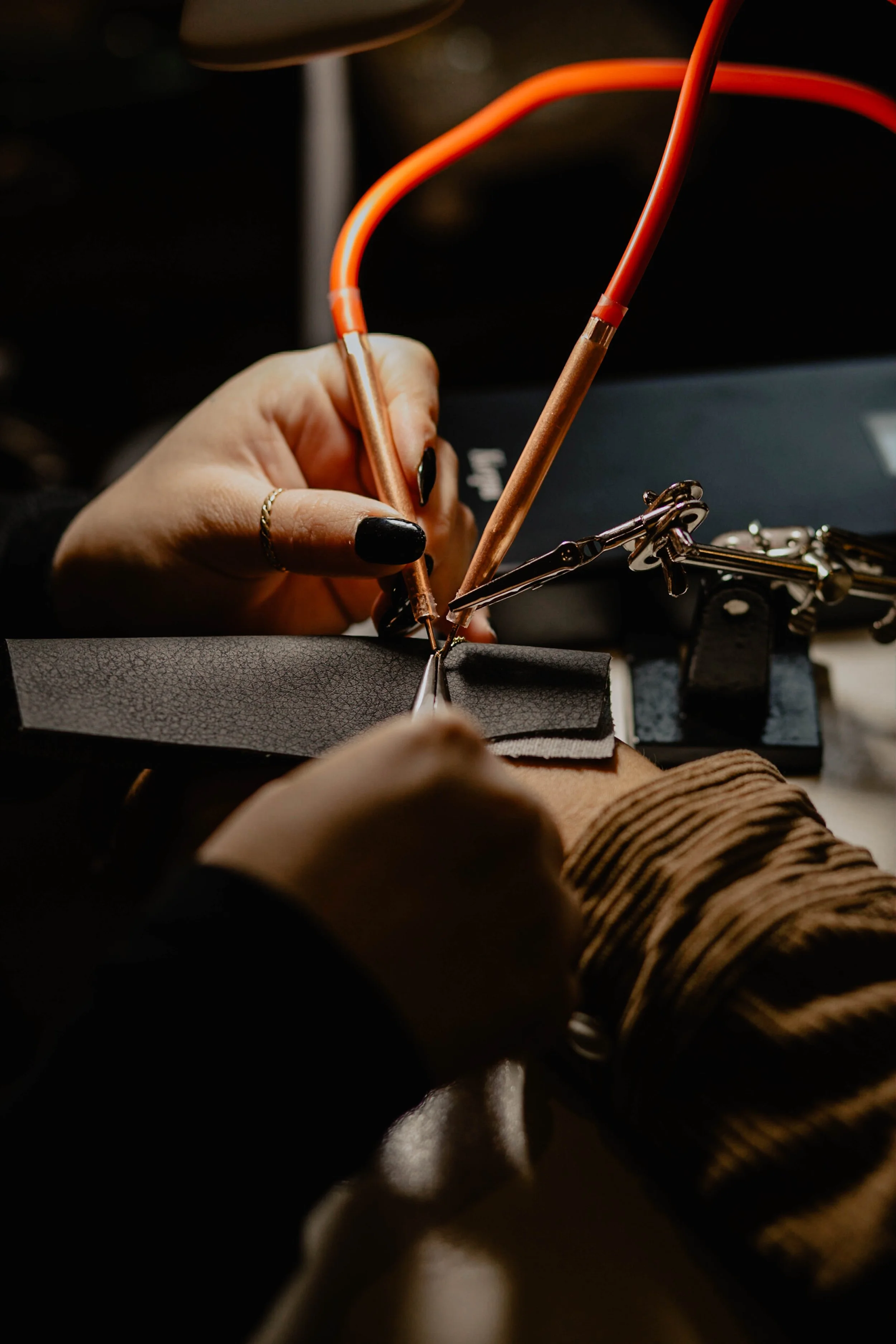 Close-up of a jeweler working on a ring, using precision tools on a leather work surface, with jewelry supplies and a laptop nearby. Seattle professional head shot photography