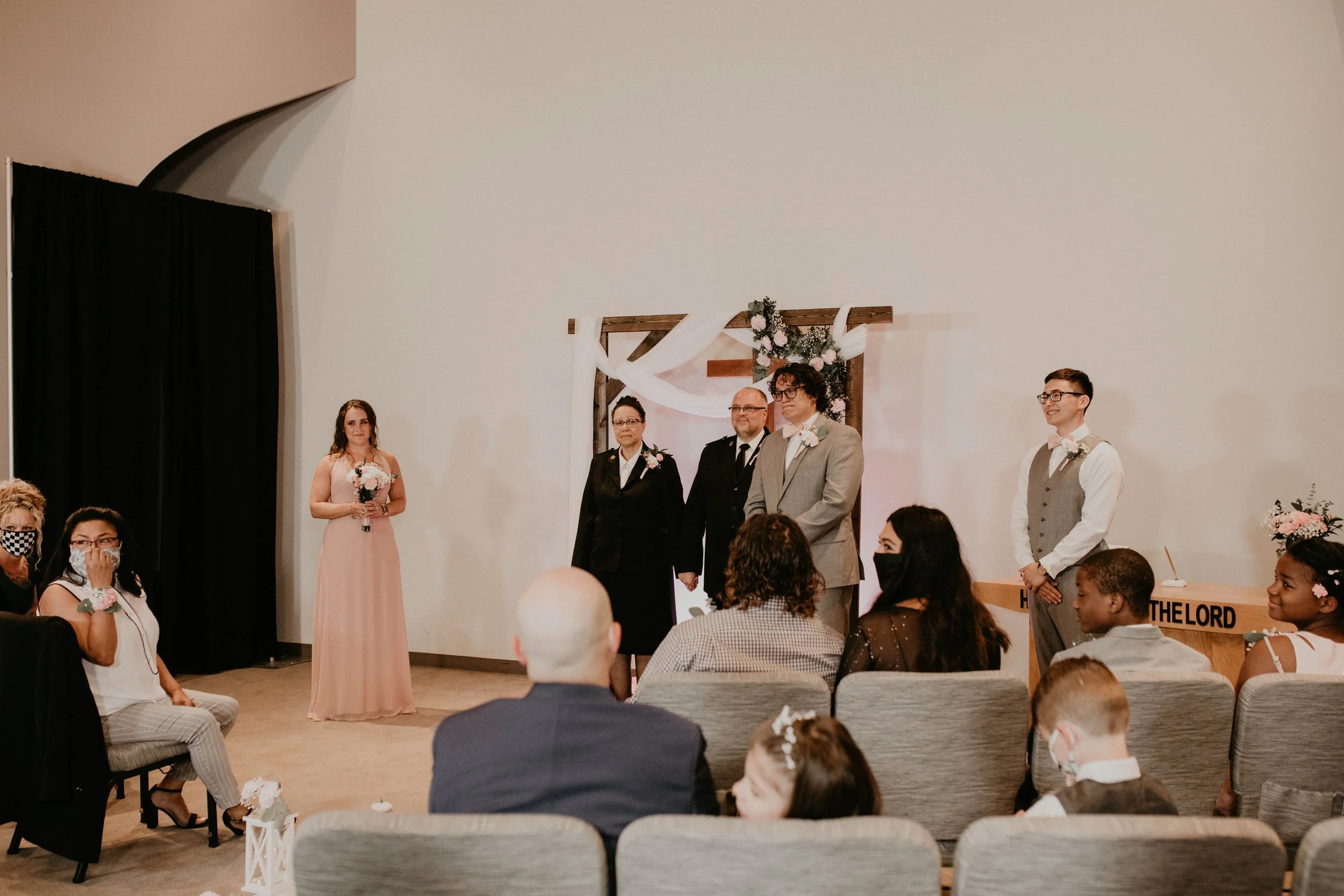 A wedding ceremony inside a church or chapel with a bride, groom, and officiant standing at the altar, surrounded by seated guests. Seattle, WA wedding photography.