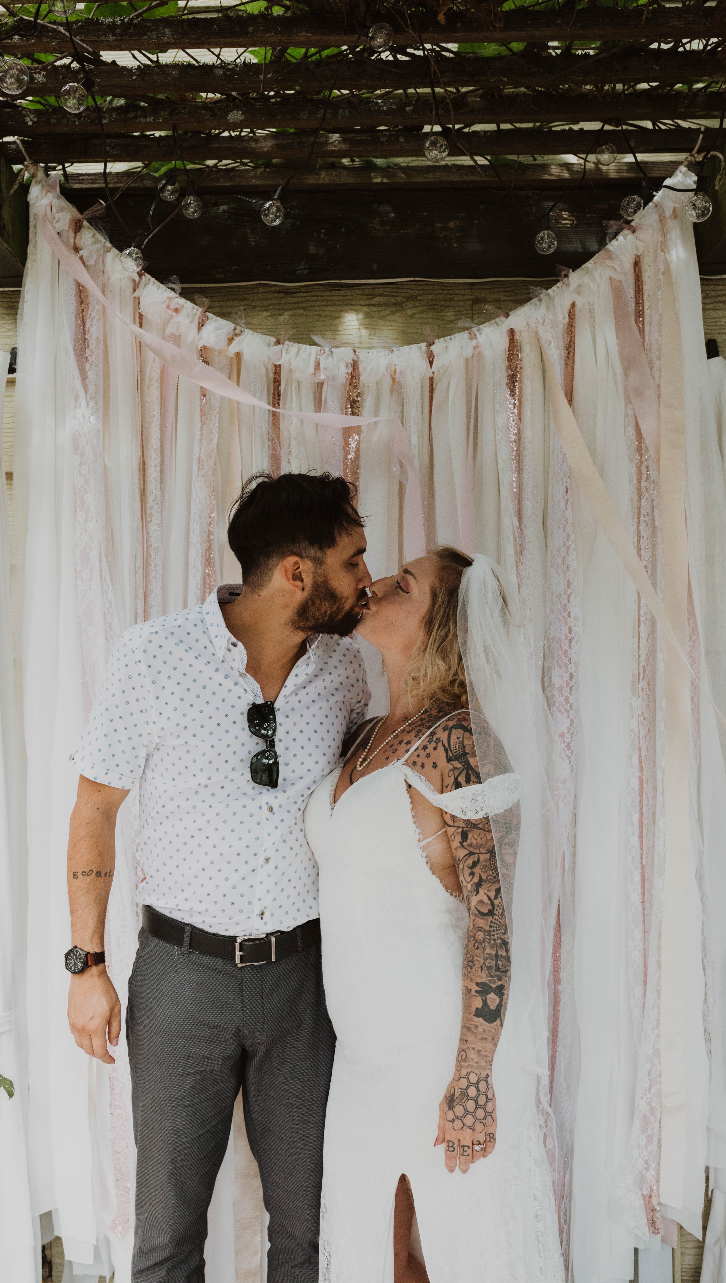 A couple sharing a kiss at their wedding, with a decorative backdrop of draped fabrics and string lights. Seattle, WA wedding photography.