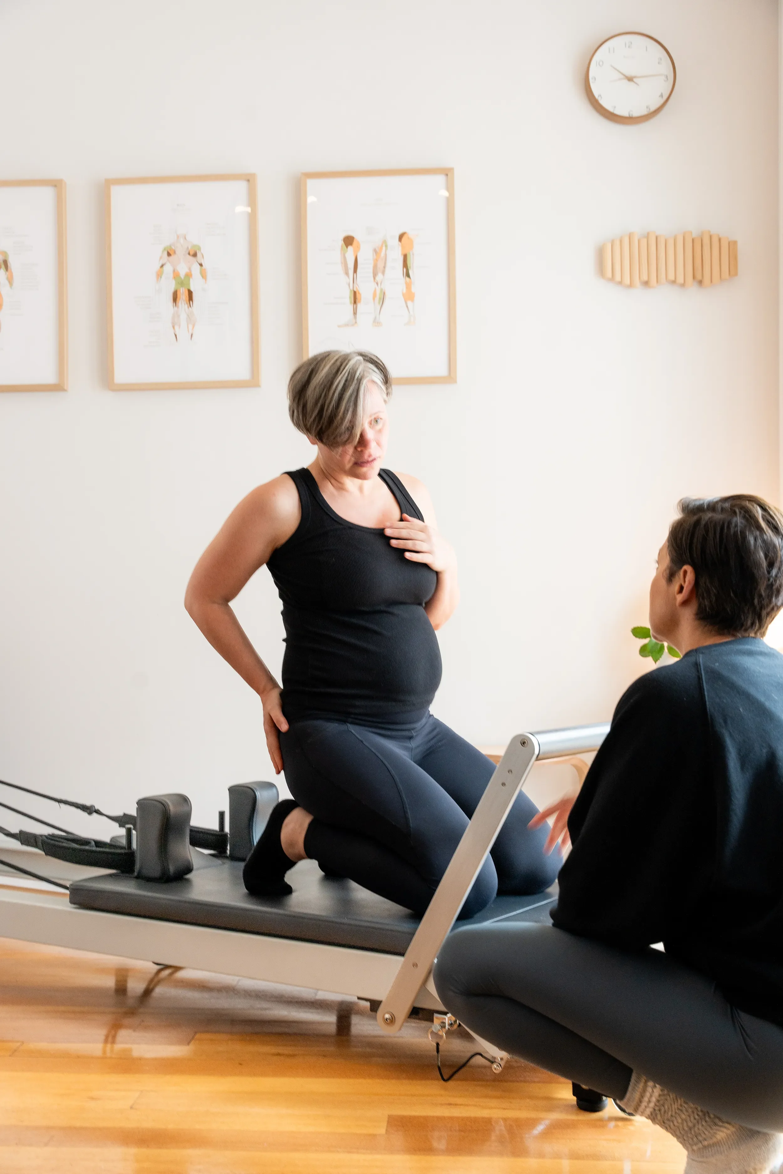 Pregnant client sitting on a reformer in discussion with Clinical Pilates practitioner Tegan Duncan during a one-to-one session in her Seddon studio.