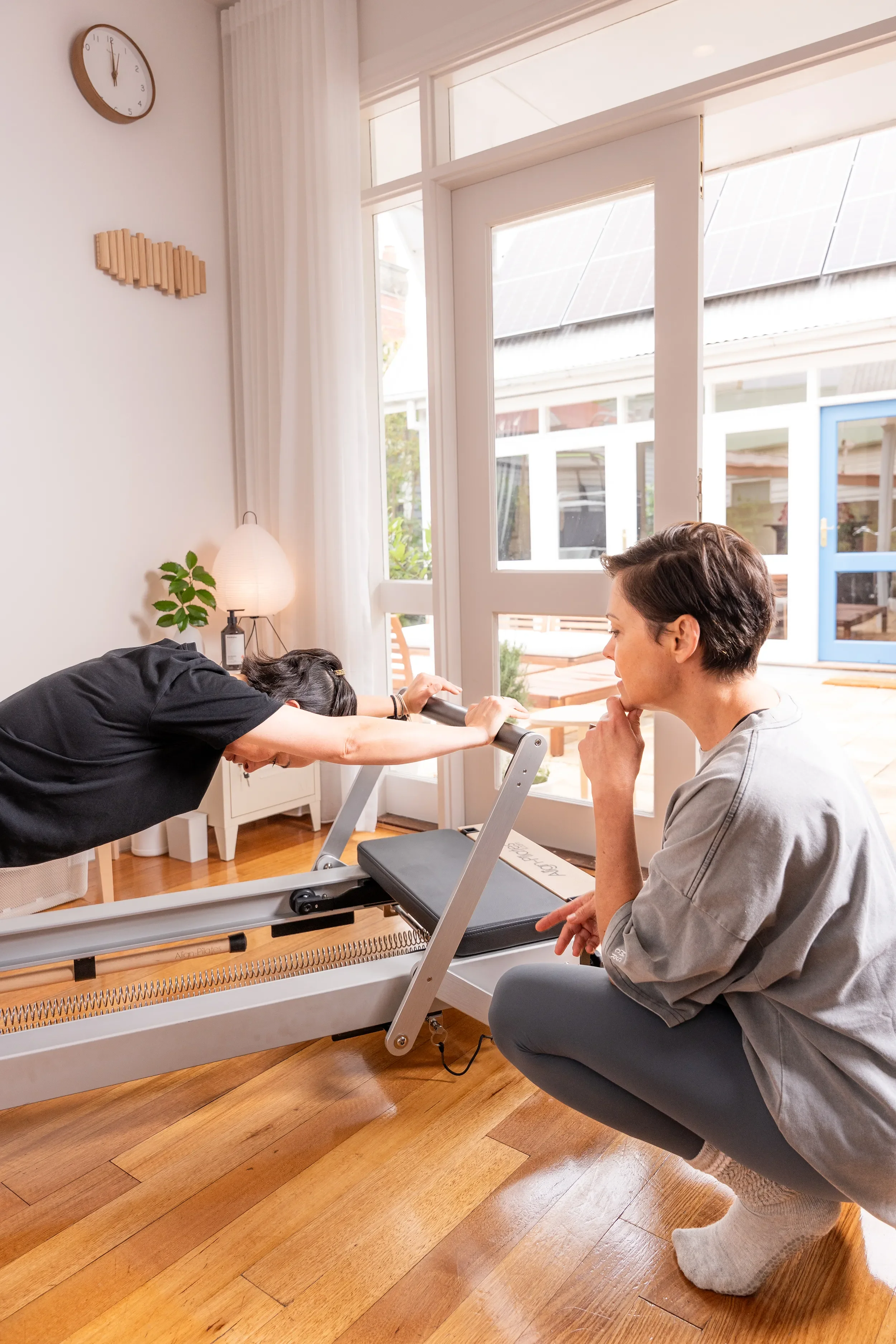 Clinical Pilates practitioner Tegan Duncan guiding a client through a supported reformer exercise in her bright Seddon studio.