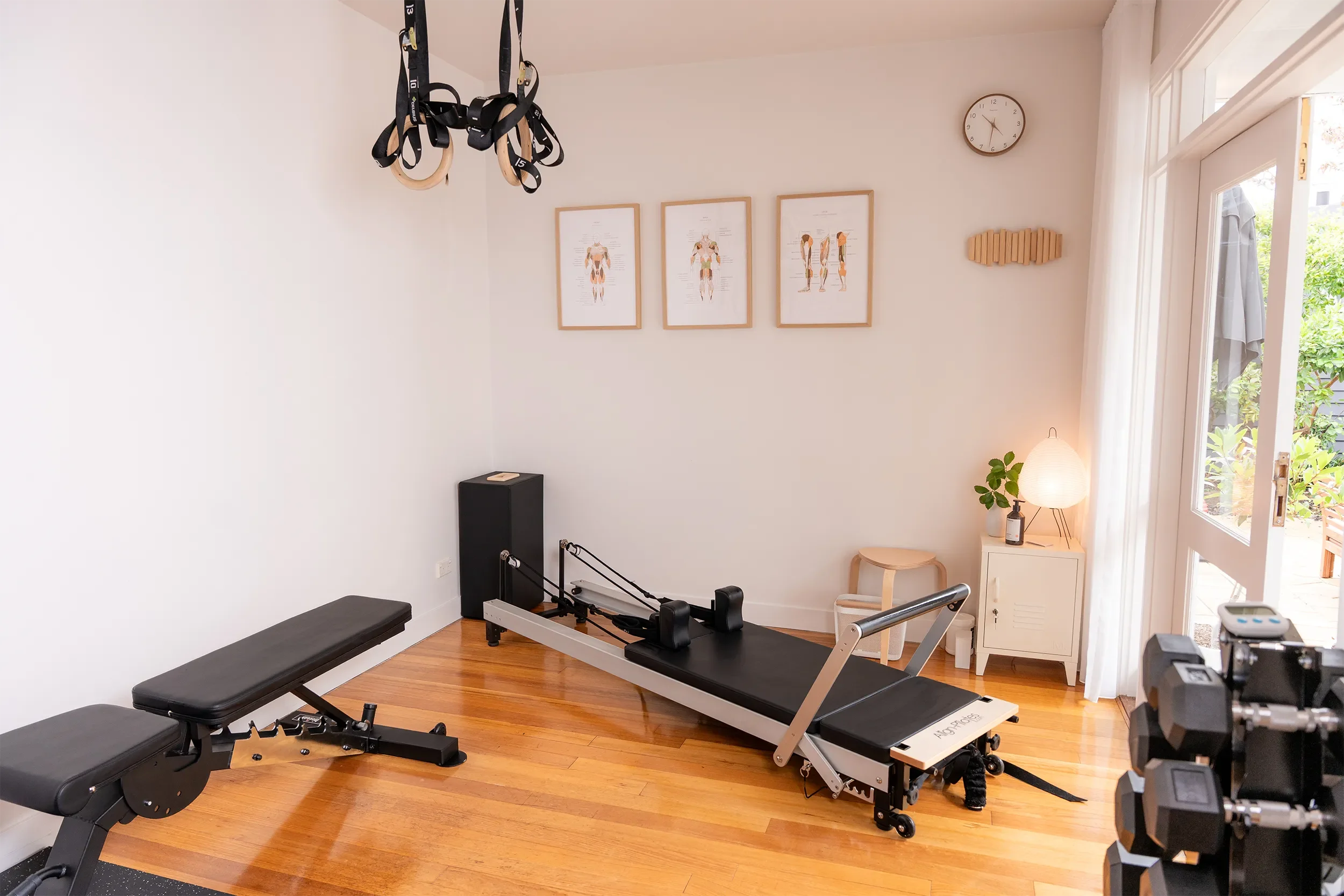Bright and welcoming Clinical Pilates studio in Seddon featuring a reformer, strength bench, dumbbells and anatomical artwork.