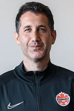 A man with short dark hair and light skin wearing a black Nike jacket with a Canada hockey logo.