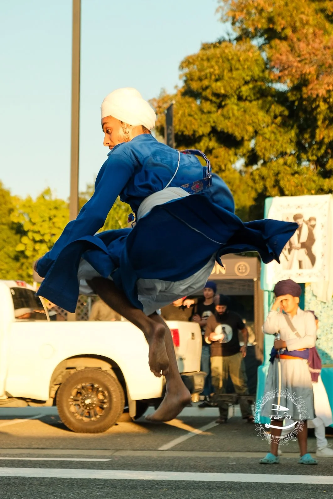 A man jumping mid-air in traditional clothing, with a crowd and trees in the background.