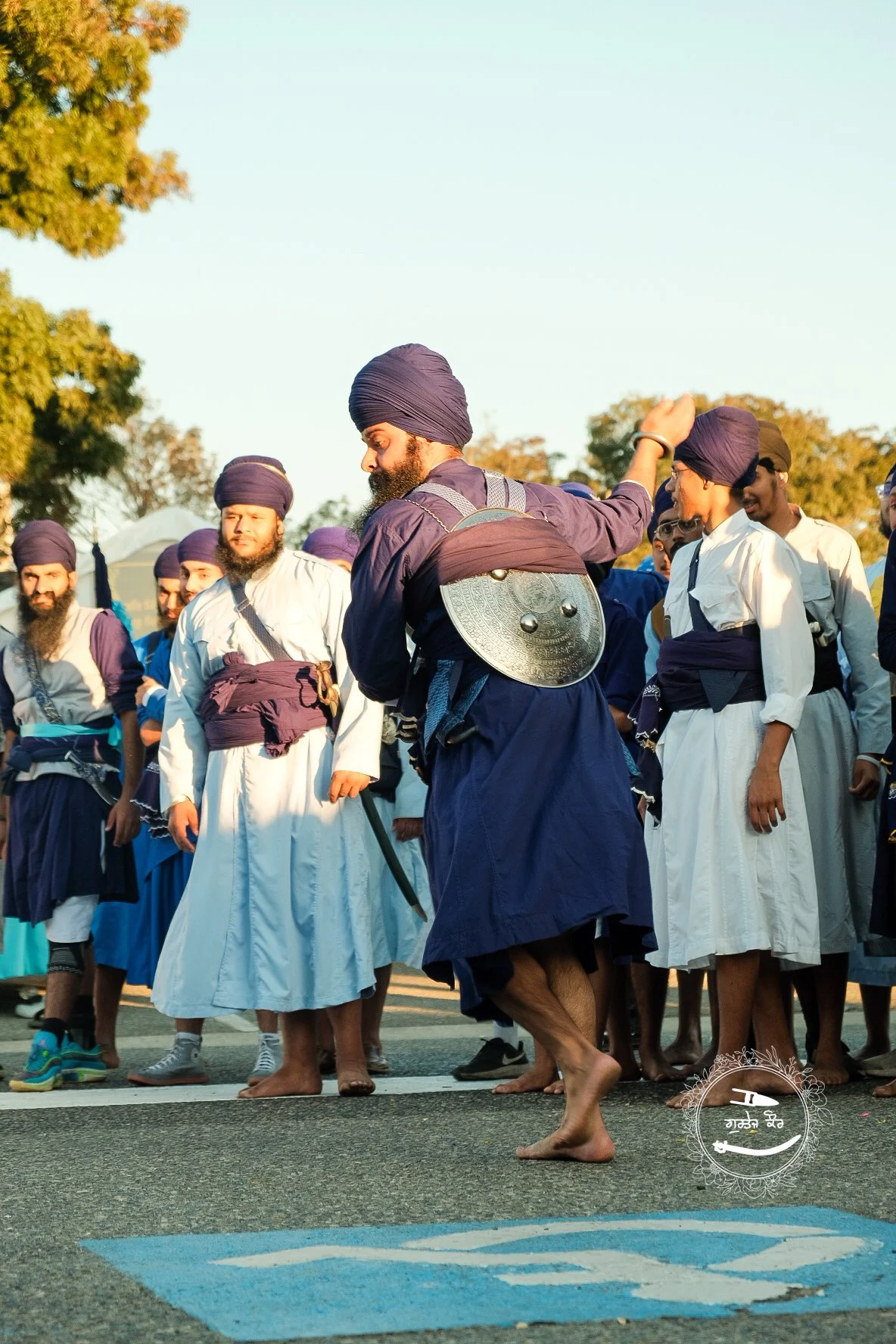 Group of Sikh men wearing traditional attire, including turbans, standing outdoors on a street during daytime, with some barefoot and others in shoes.