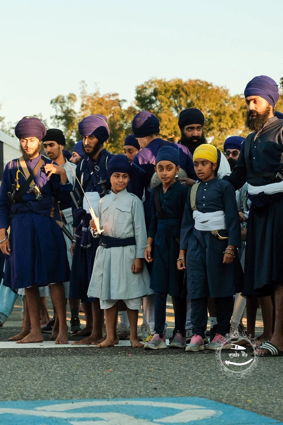 Group of Sikh men and children dressed in traditional attire, some holding lit candles, gathered outdoors during sunset.