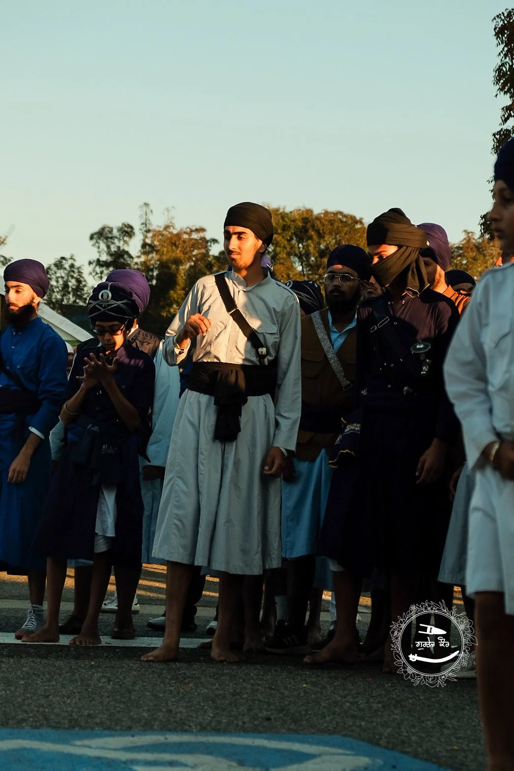 Group of young men dressed in traditional Sikh clothing, including turbans, standing outdoors during late afternoon or early evening.