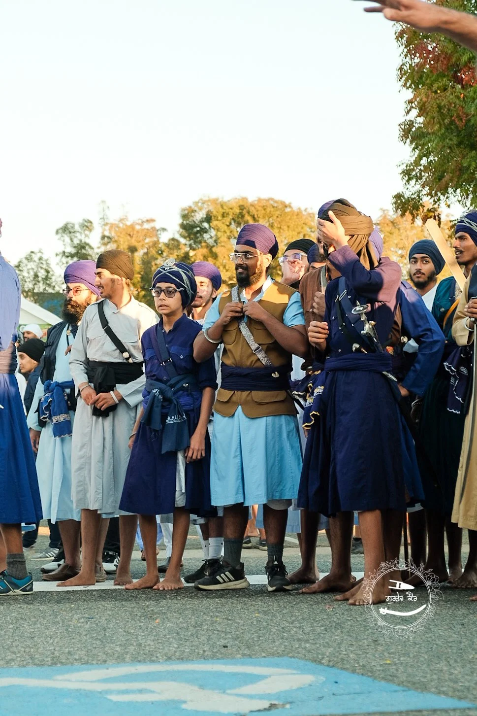Group of Sikh men and women in traditional attire, standing outdoors, possibly during a festival or gathering.