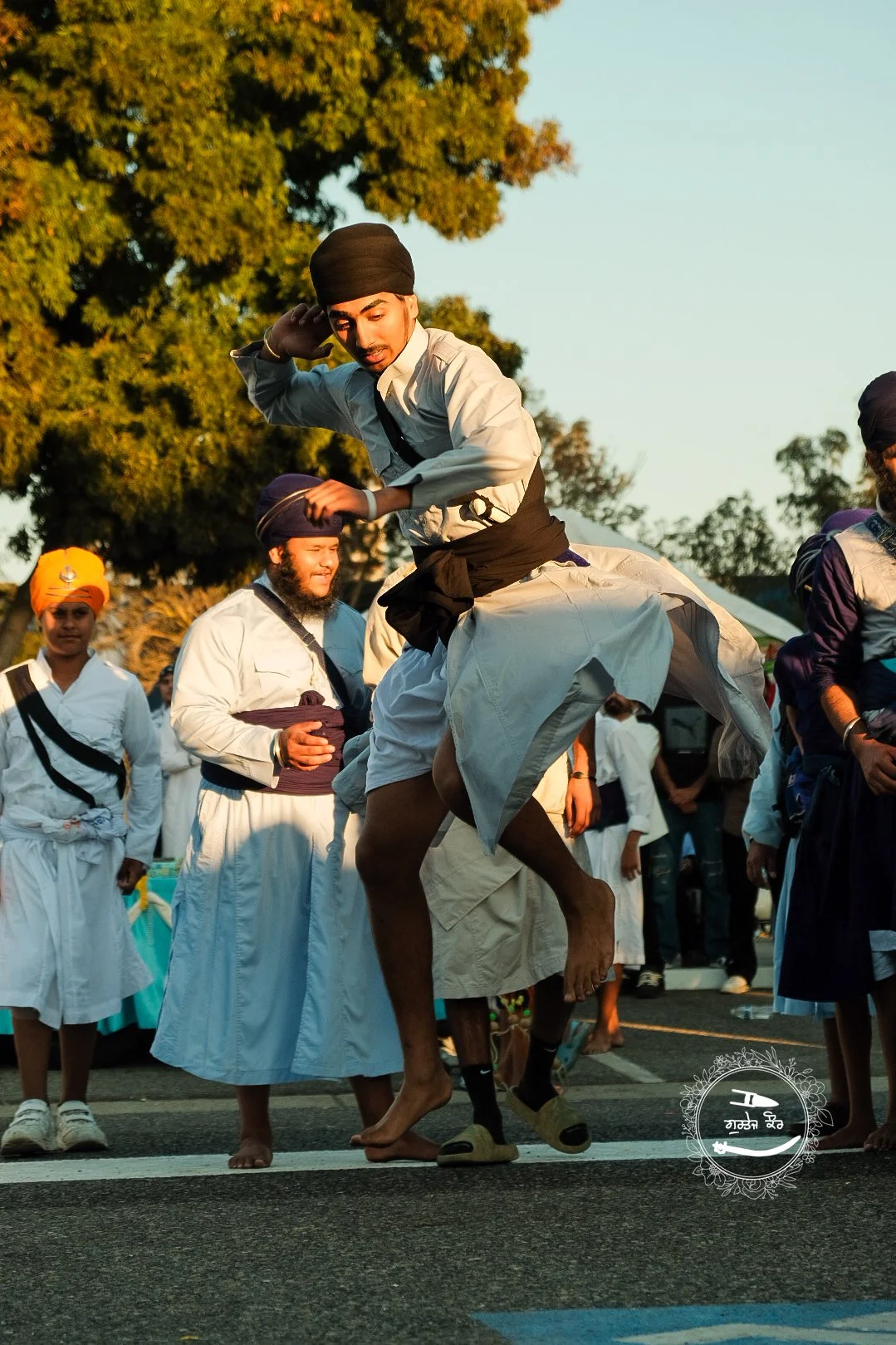 Man dressed in traditional Sikh attire answering a question in a crowd of people, some wearing turbans, standing outdoors during a festival or celebration.