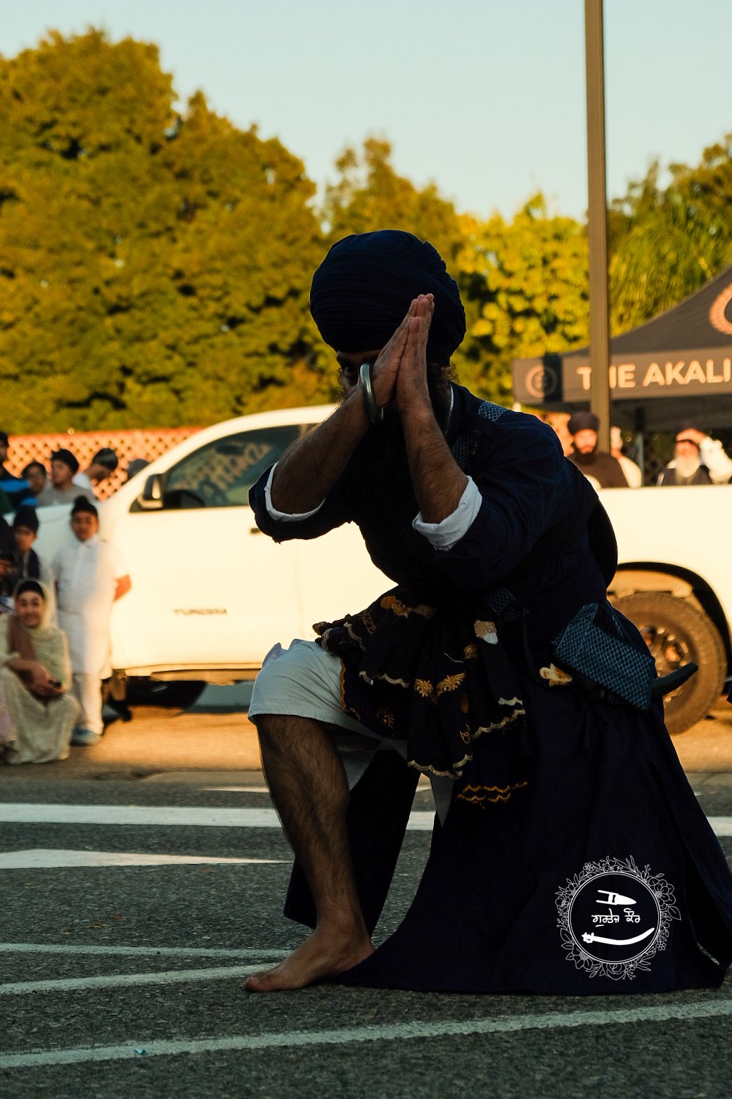 A man in traditional attire performing a traditional Indian dance on the street during a cultural festival, with onlookers watching in the background.