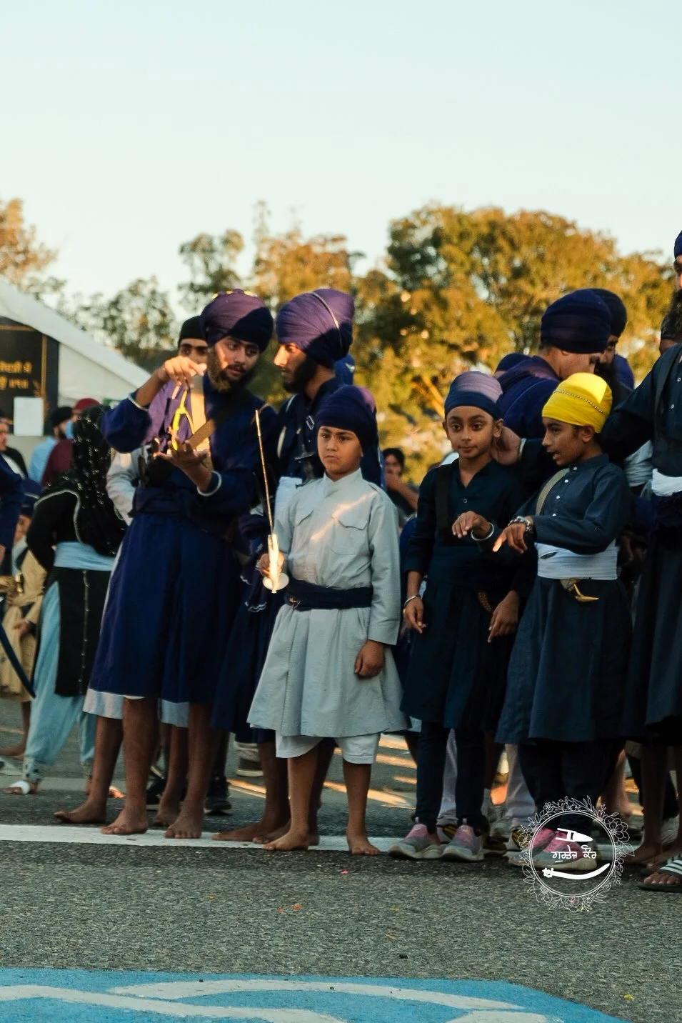 Group of young boys and men dressed in traditional Sikh attire, including turbans, standing together outdoors during sunset.