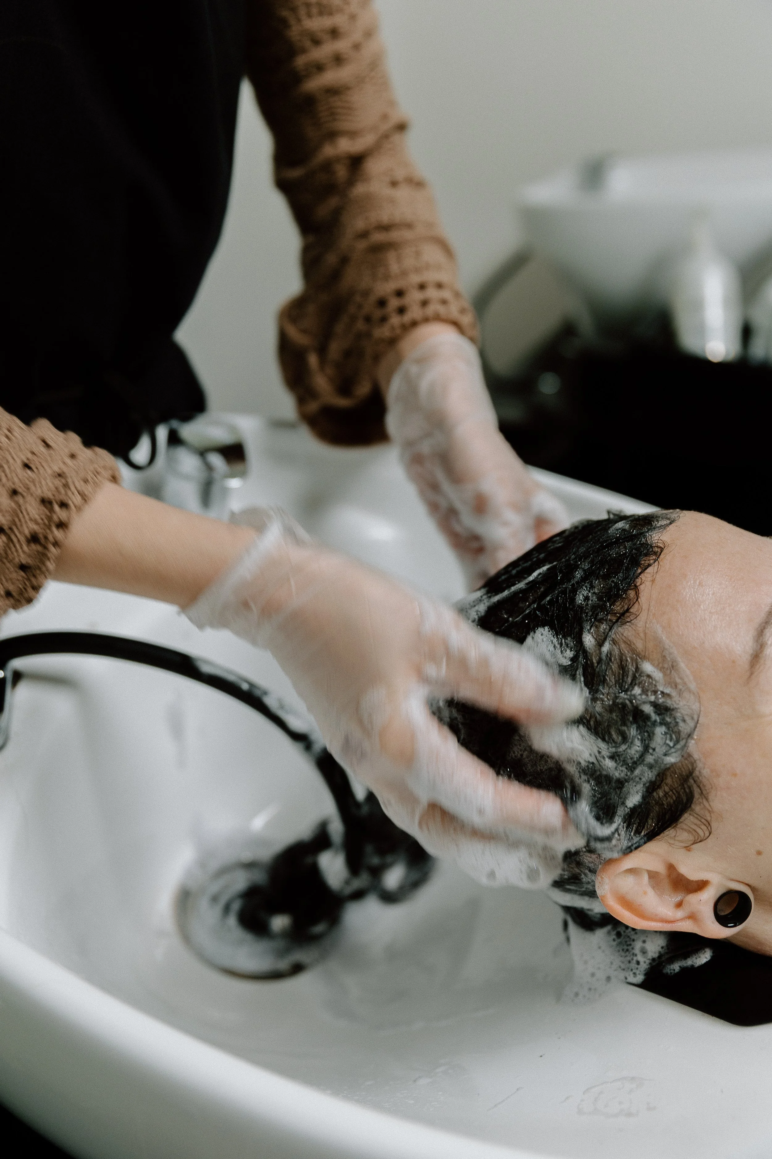 Person washing hair in a salon sink with bubbles and shampoo lather.