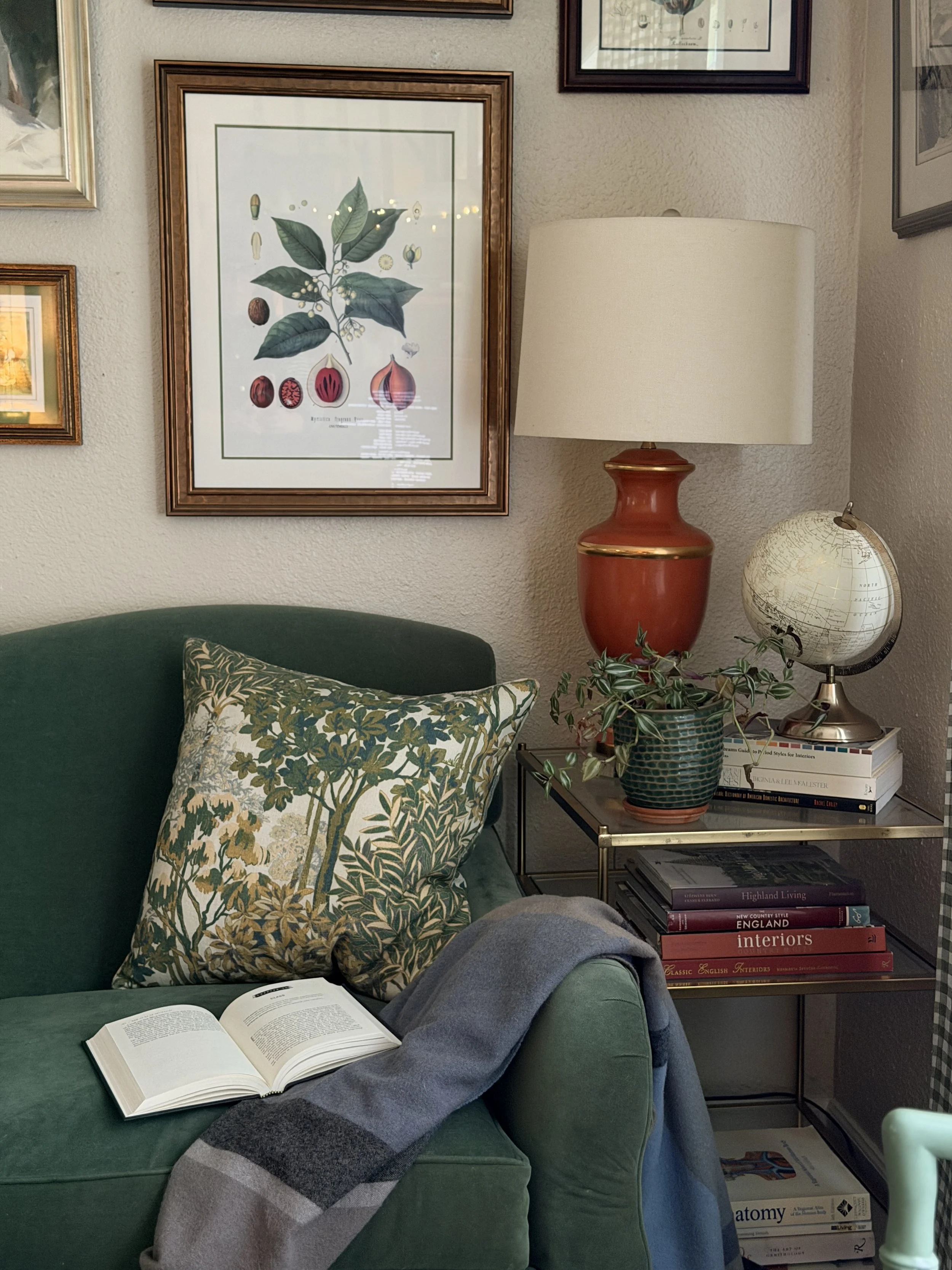 Living Room corner with table and lamp, lots of art on the walls, and sofa with a blanket and book.