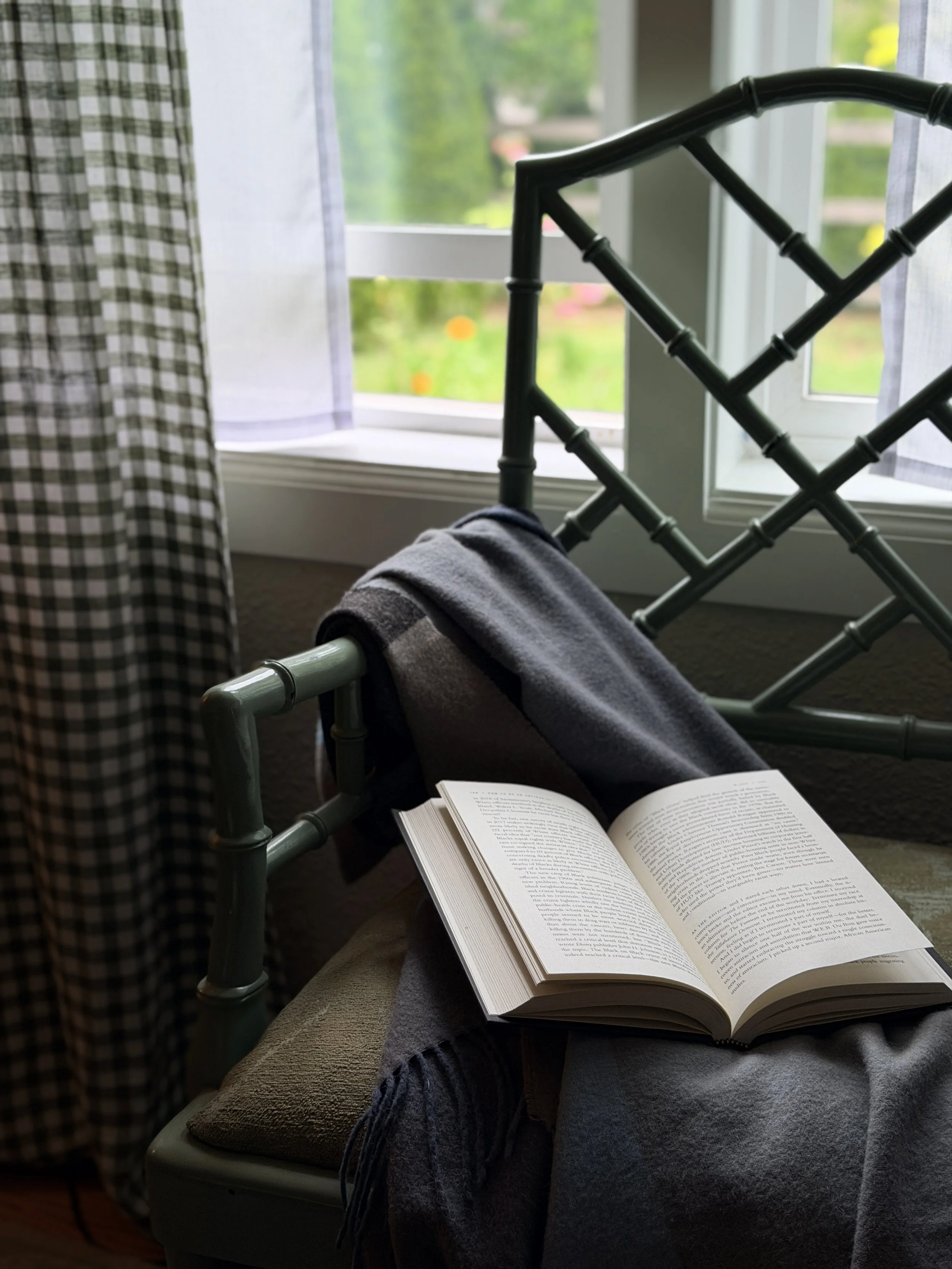 Open window, curtain blowing, chair with open book and blanket