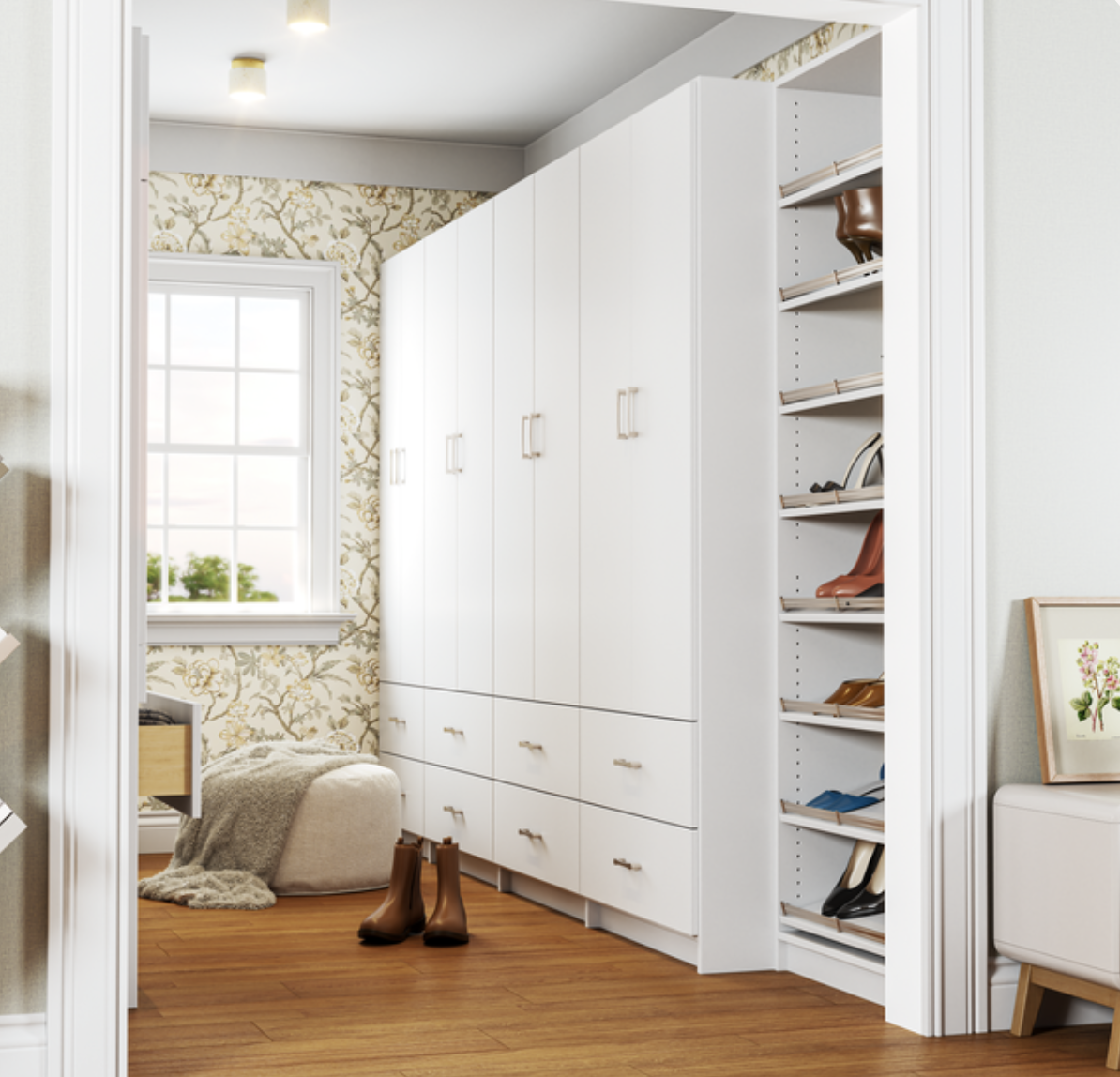 View of a bedroom wardrobe with white cabinetry, some open shelves with shoes, a chair with brown boots in front, a window with a partly cloudy sky visible outside, a small bed or seating area with a blanket and pillow, and a wood floor.