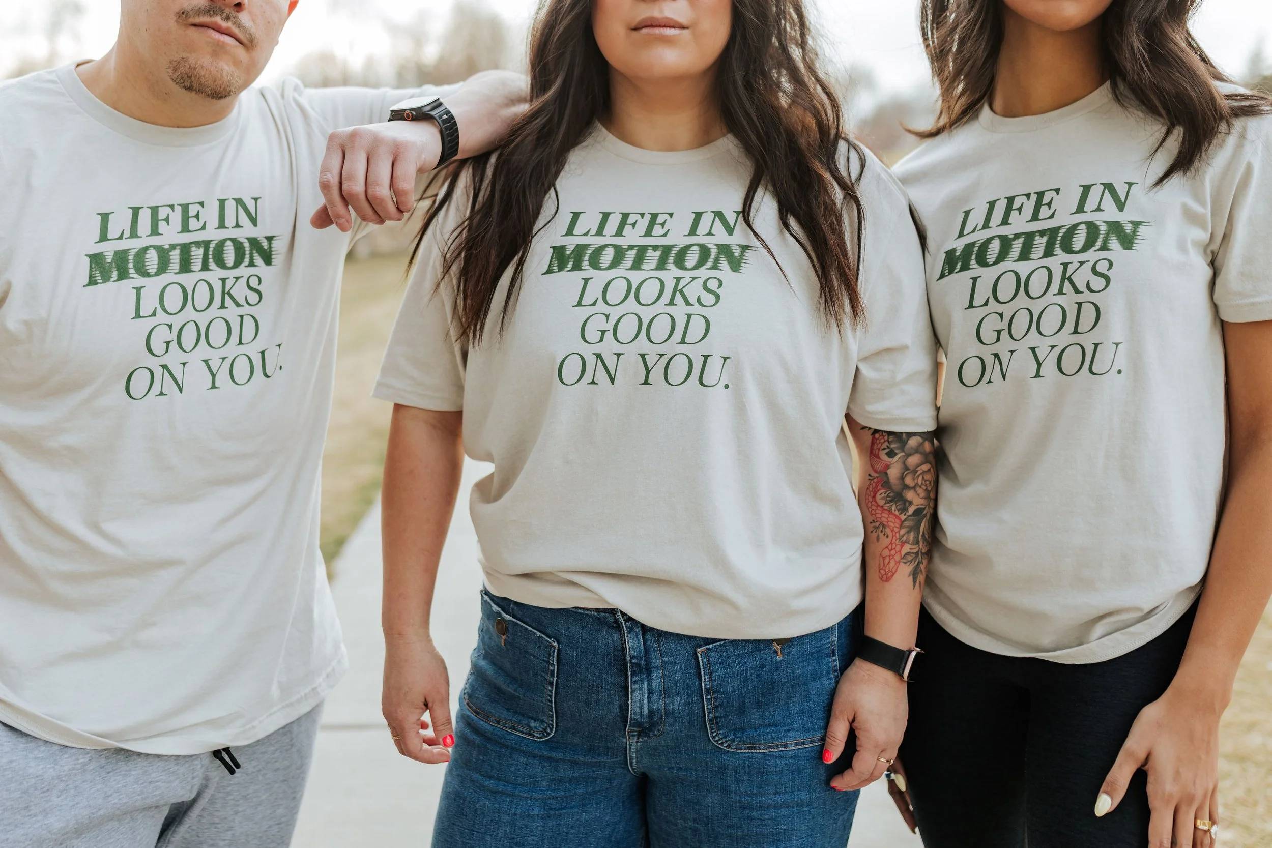 Three people standing wearing the life in motion tee 