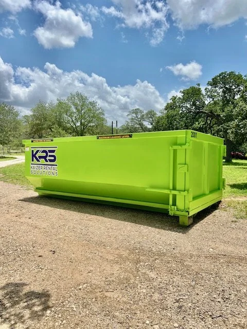Bright green rental container with logo and text, parked on gravel ground with trees and blue sky with clouds in the background.