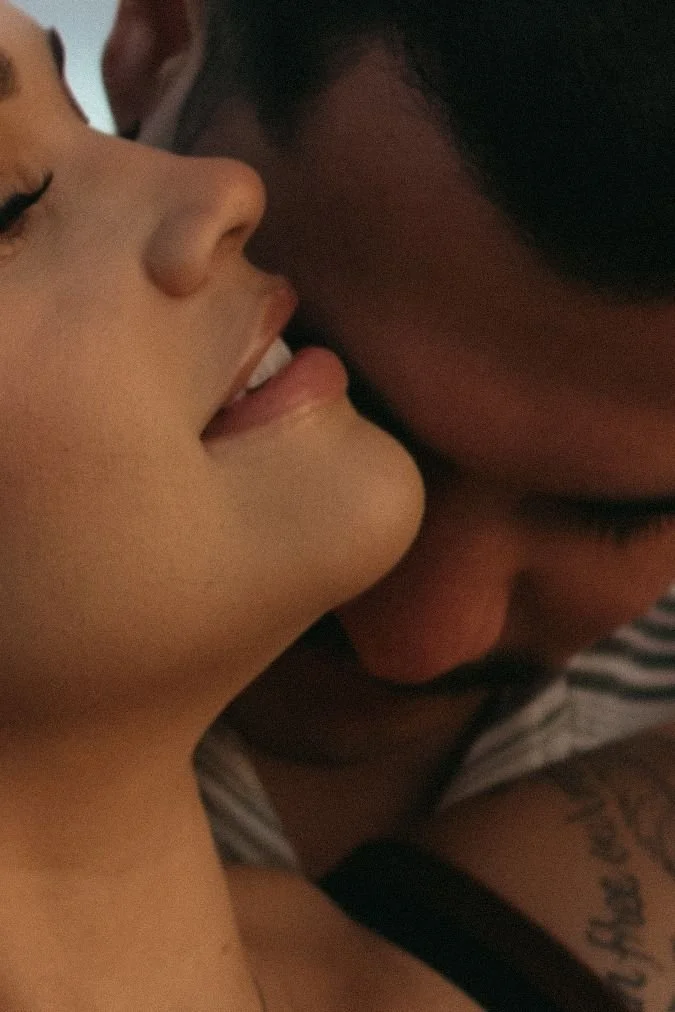 Close-up of two people in an intimate moment, with one person's face near the other's neck and lips close to their face.