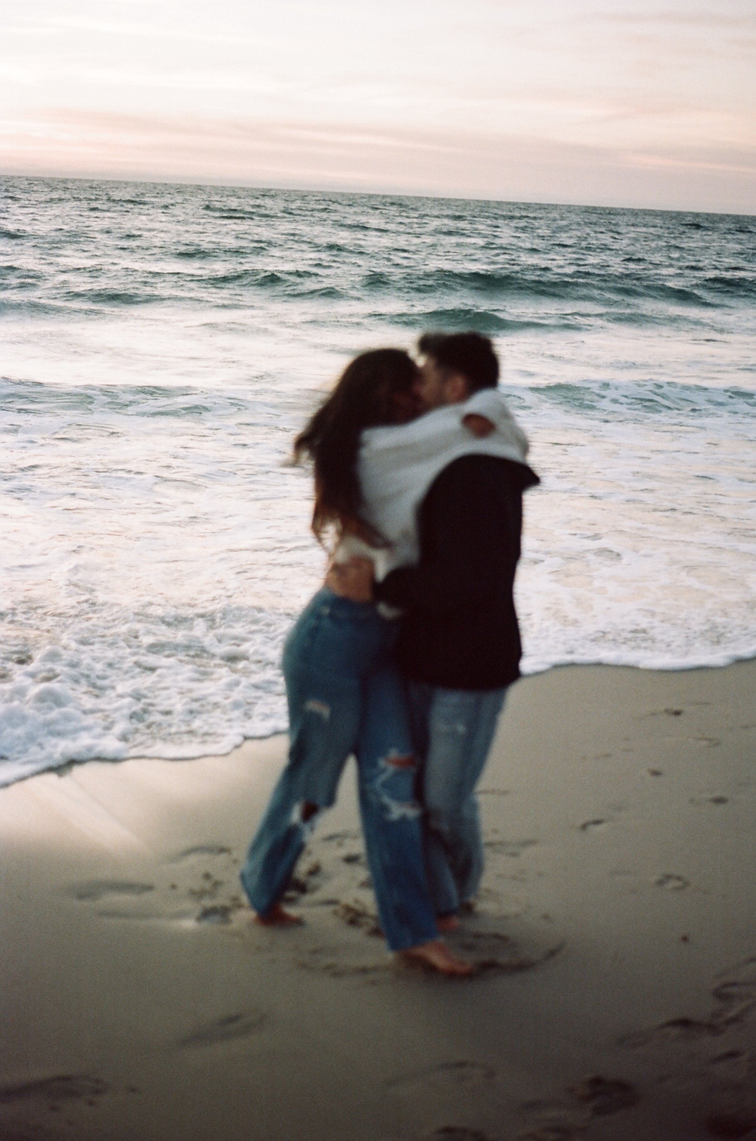 A couple embracing on the beach near the ocean at sunset